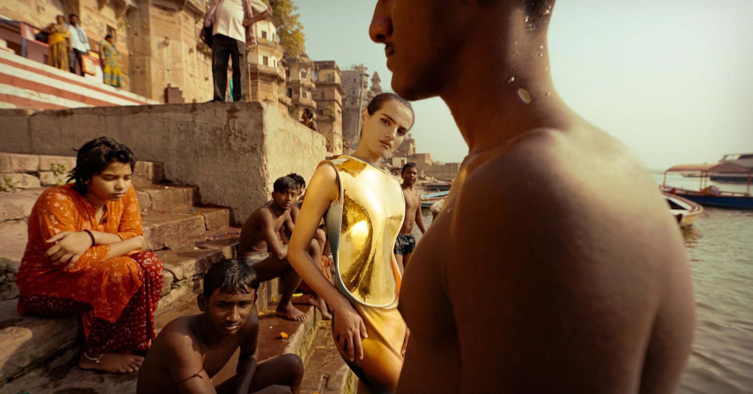 A woman wearing a gold dress with a group of people sat on steps by a river.