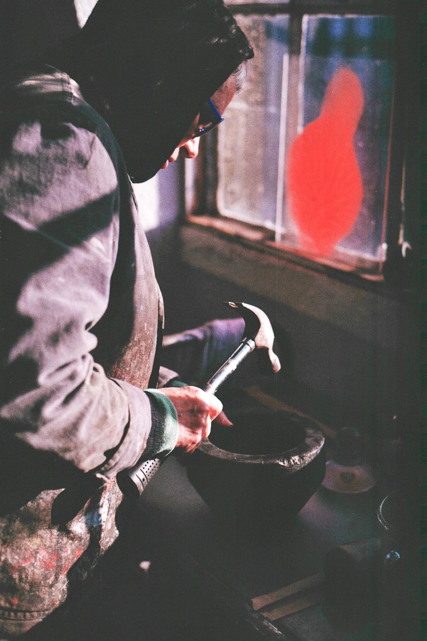 Person in cap and light jacket sits holding curved tool, facing screen displaying bright red shape against dark background.
