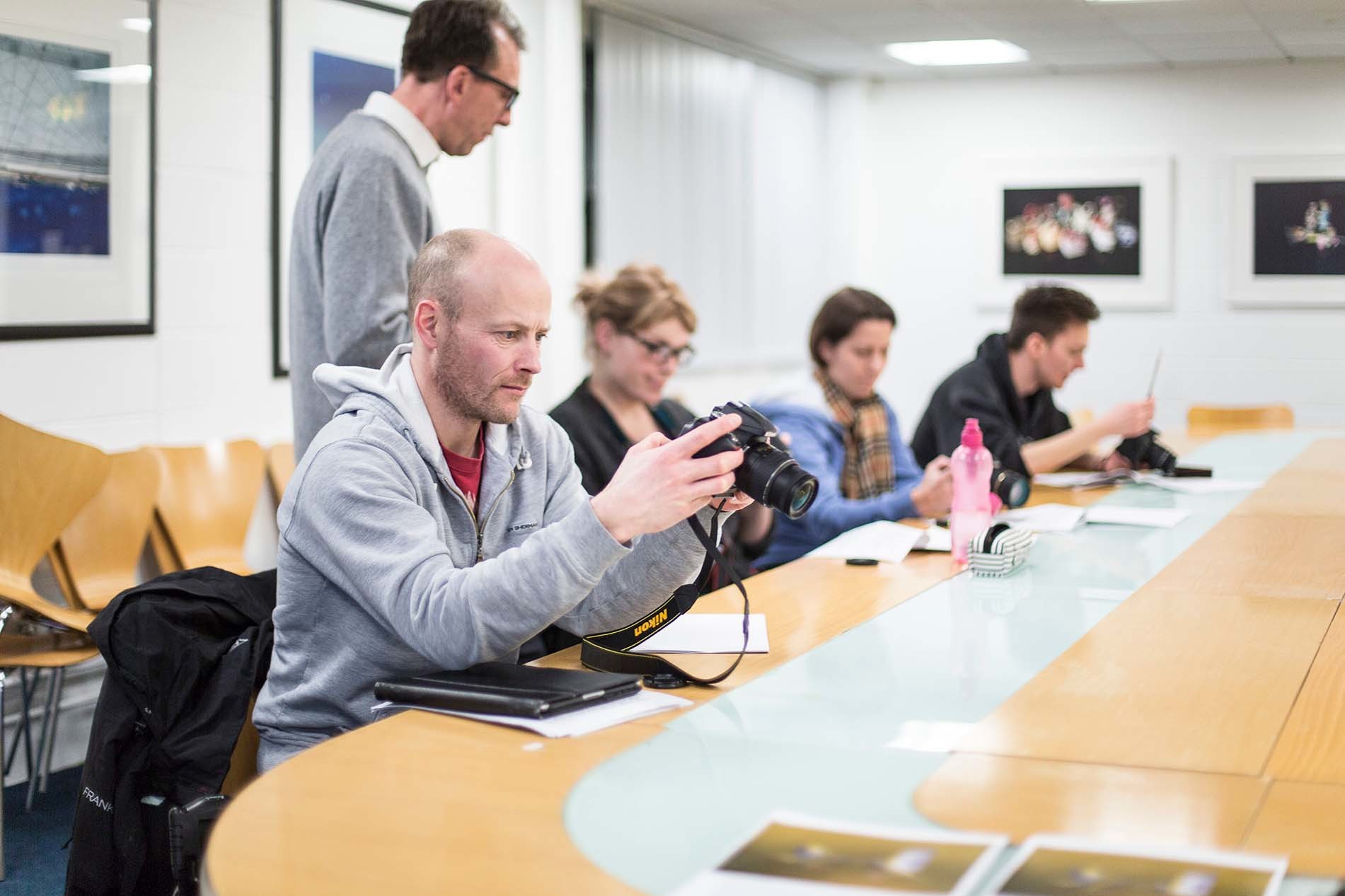 Four people sitting around a table in a classroom with cameras in front of them.
