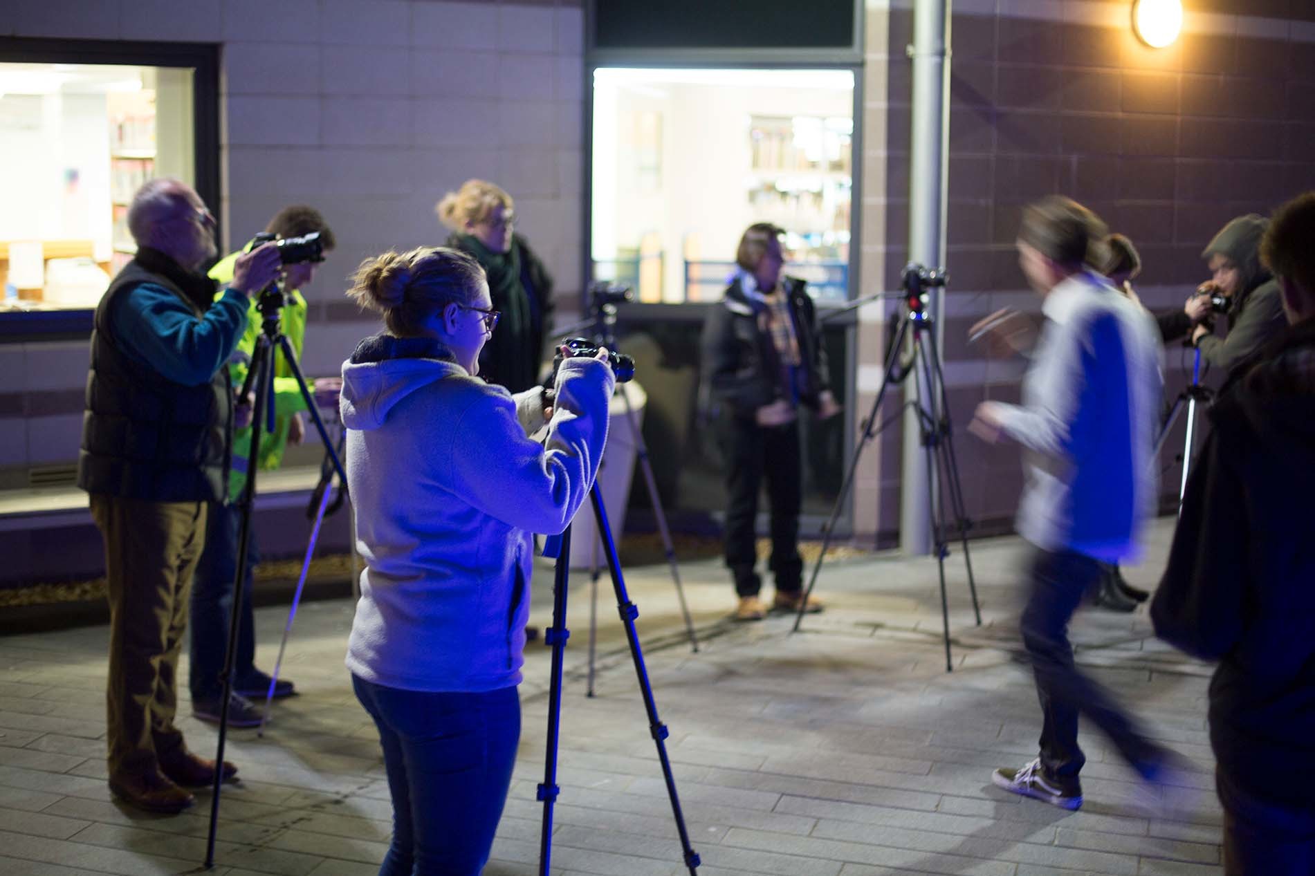 A group of people standing in a university courtyard at night, all with cameras and tripods.