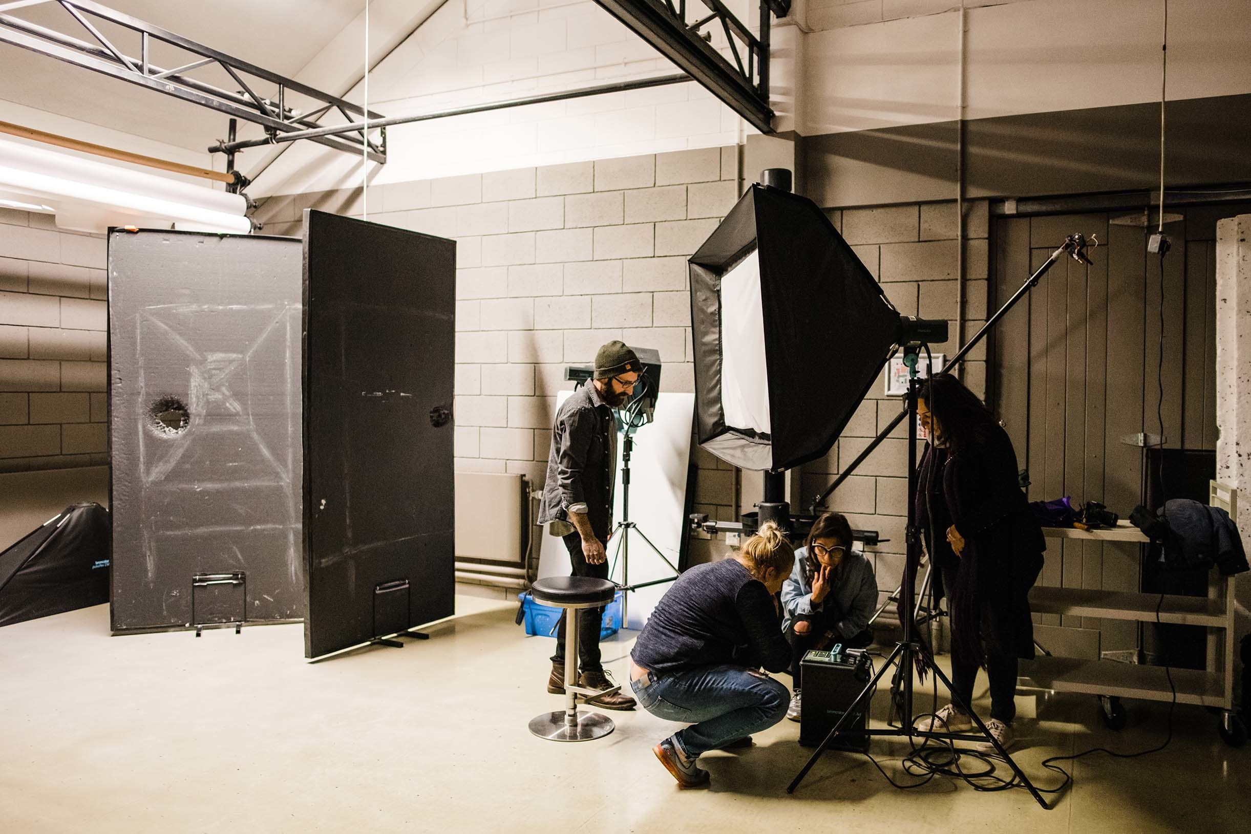 Four people in a photography studio, examining a box near a lighting box and stand.