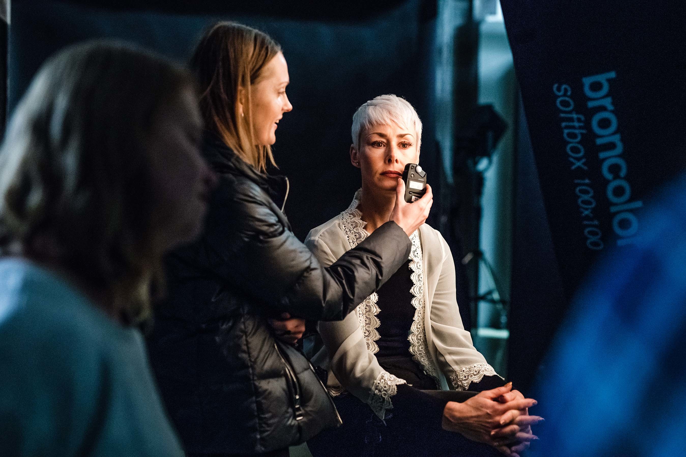 A person holds a piece of equipment up to a model's face in the middle of a photo shoot.