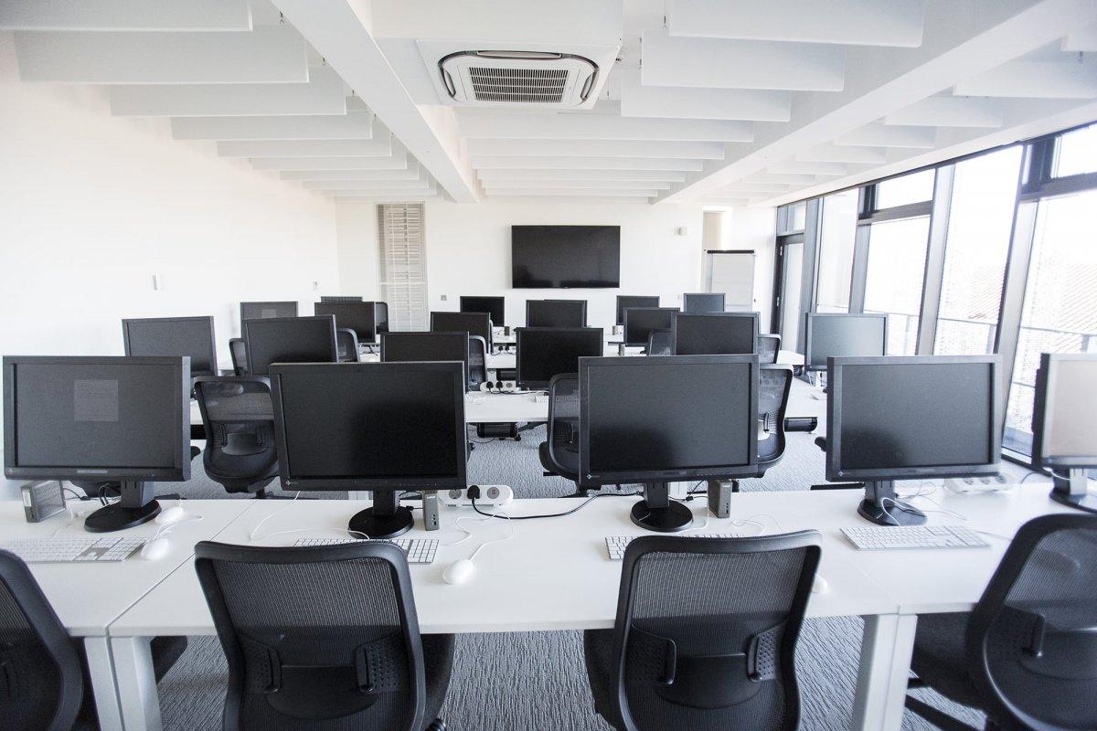 Four banks of desks in a computer suite with monitors on them.