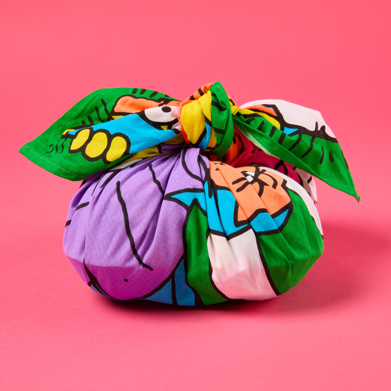 Multicoloured, pattered Lush Knot Wrap on a bright coral pink/red background.