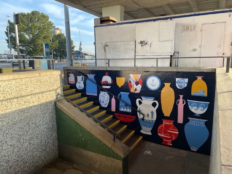 A mural of different vases and bowls on a wall next to some steps leading to a train station.