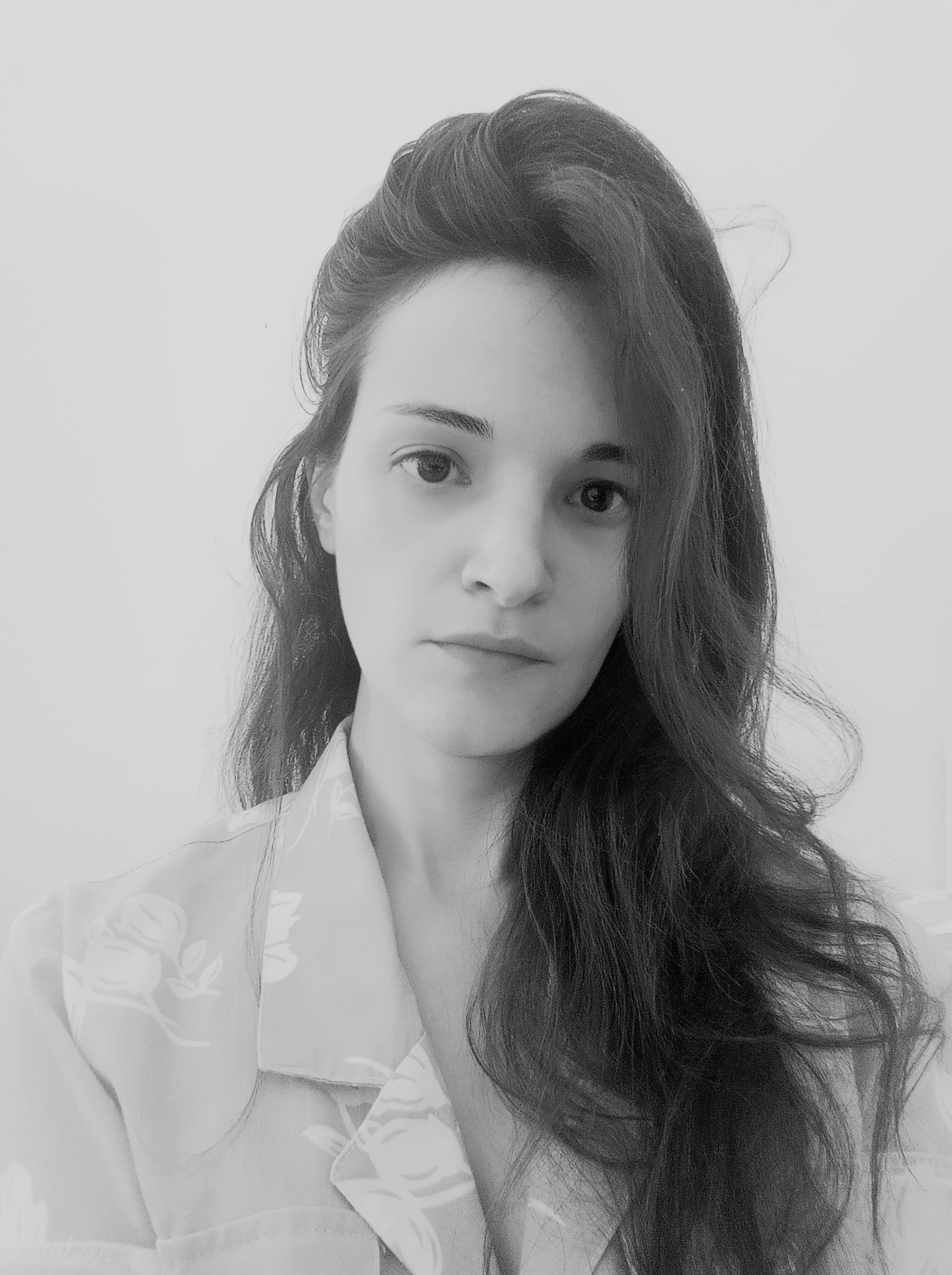 Black and white portrait of woman with long wavy hair wearing white collared shirt, looking directly at camera against plain background.