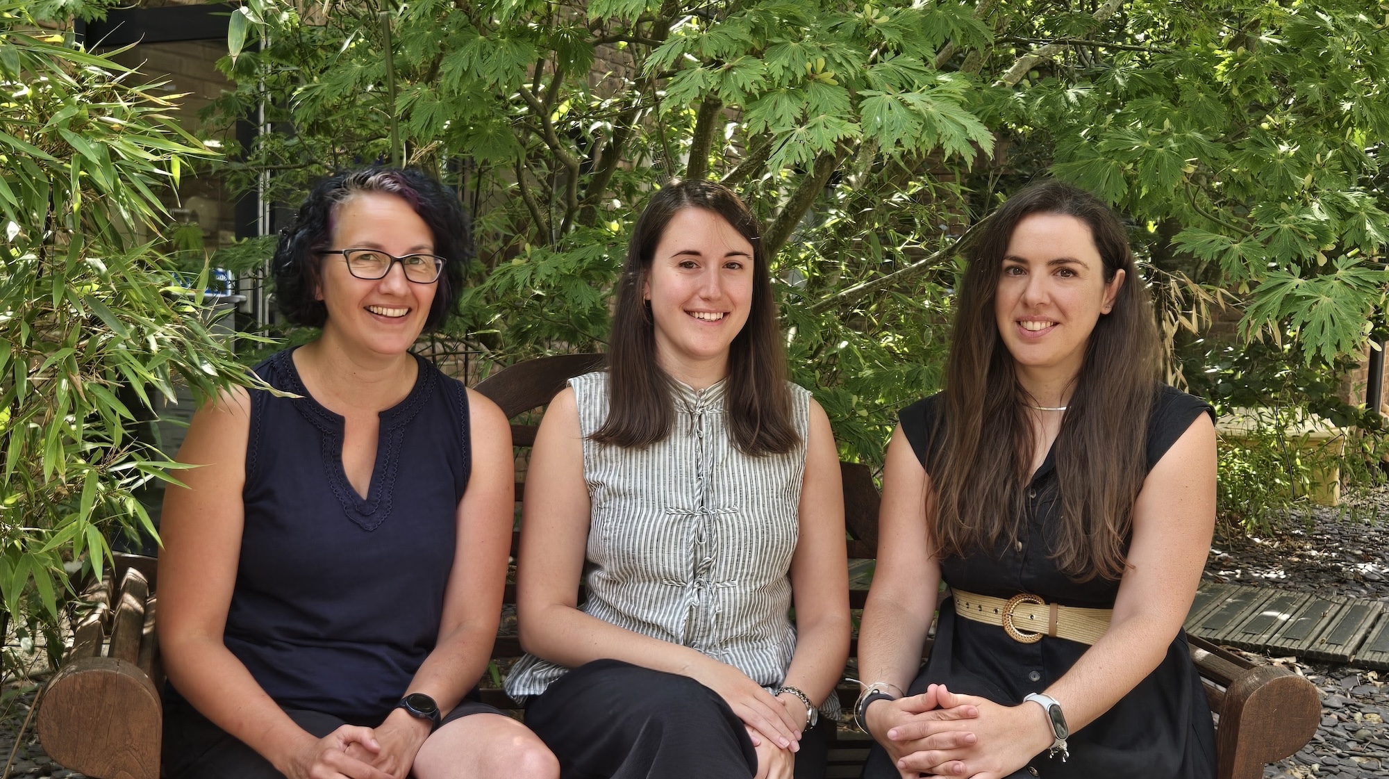 Three members of Arts University Bournemouth research staff sitting and posing for a photo with greenery in the background.