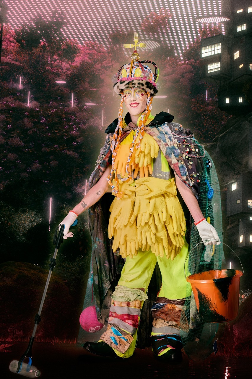 Person in elaborate yellow costume with ornate headdress, standing under pink geometric ceiling with urban backdrop at night.
