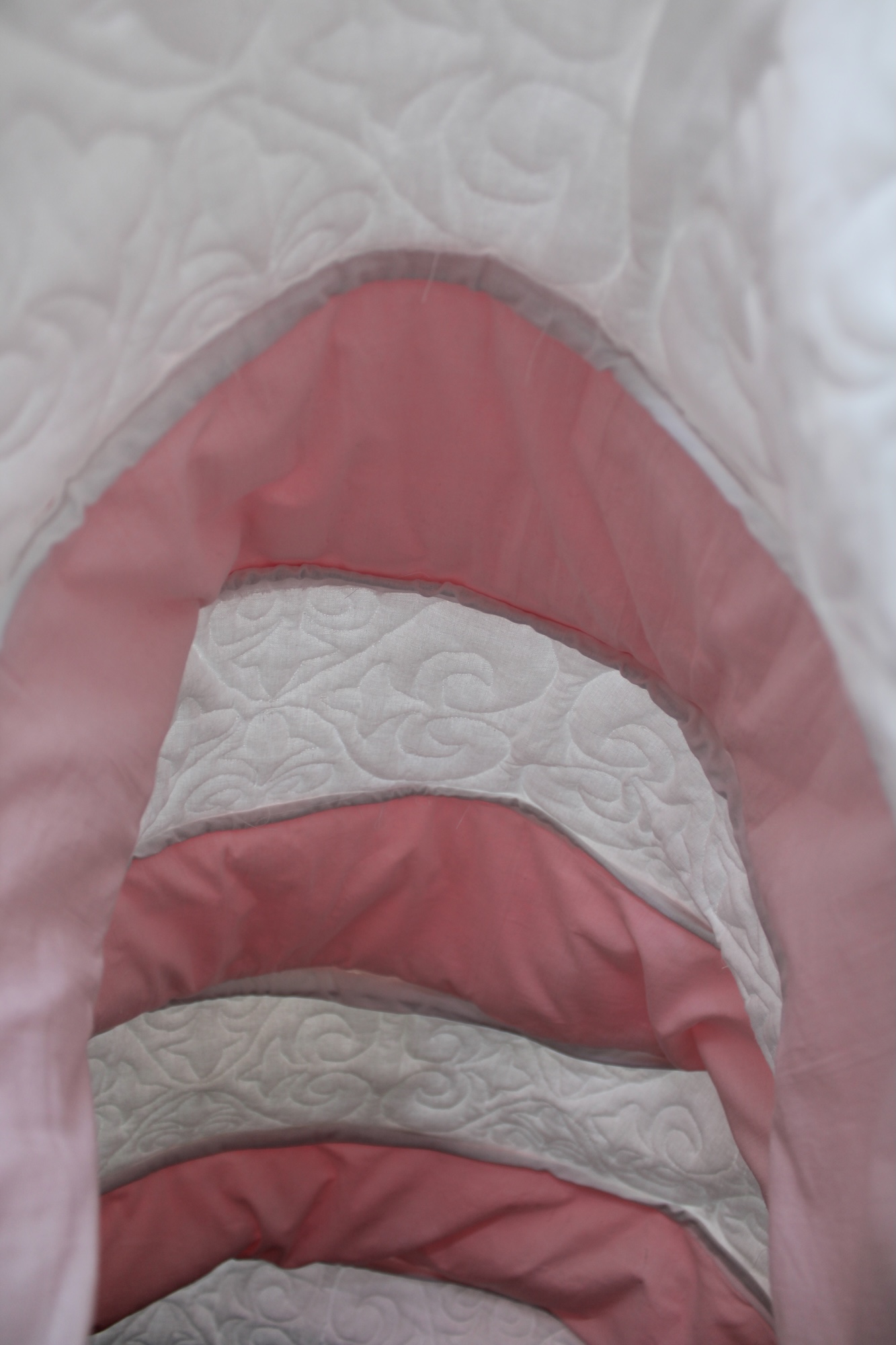 A close-up of a white quilted fabric with pink curved bands running vertically through the centre.
