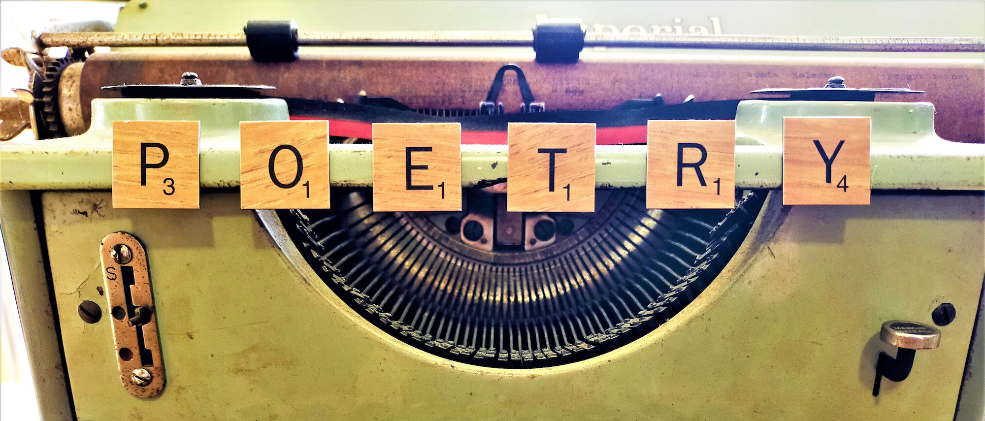 Top of a typewriter and Scrabble tiles arranged to spell 'Poetry' above it.