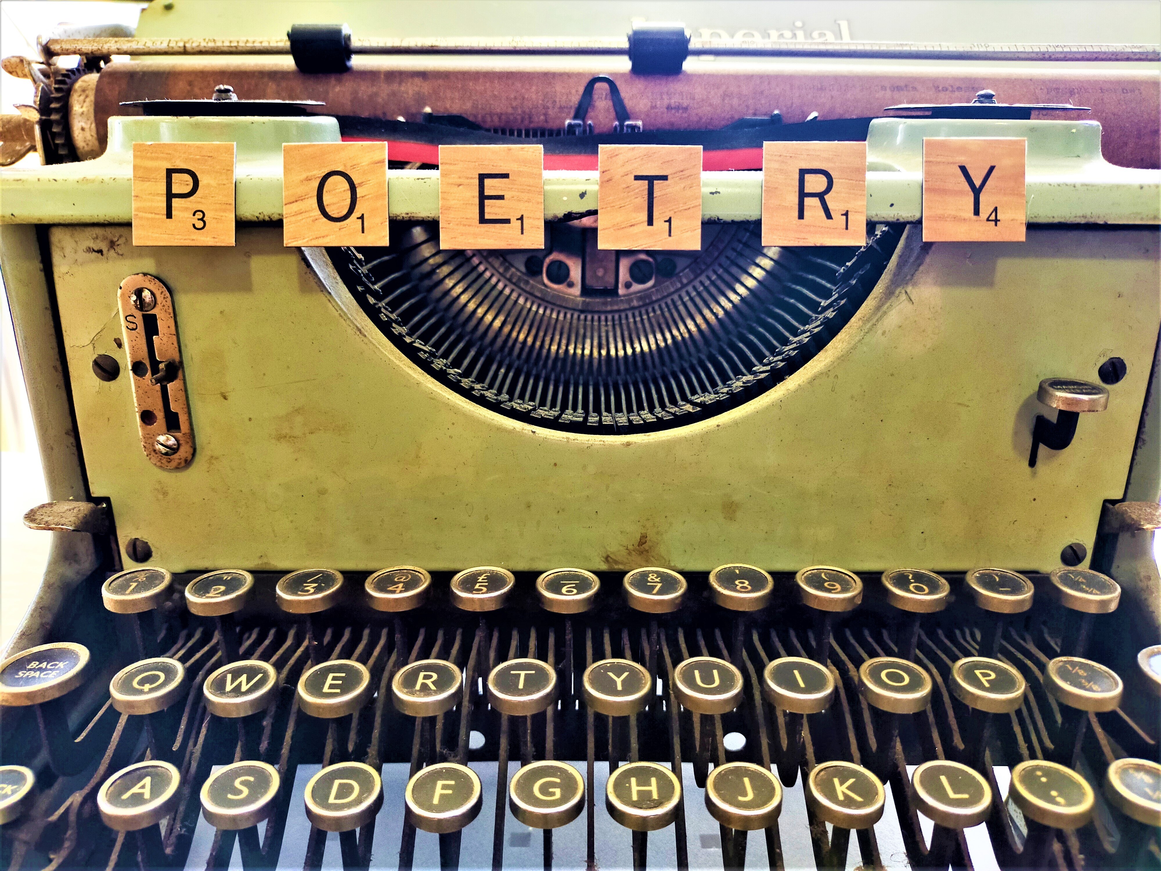 Close-up of a typewriter and keys with Scrabble tiles arranged to spell 'Poetry' above it.