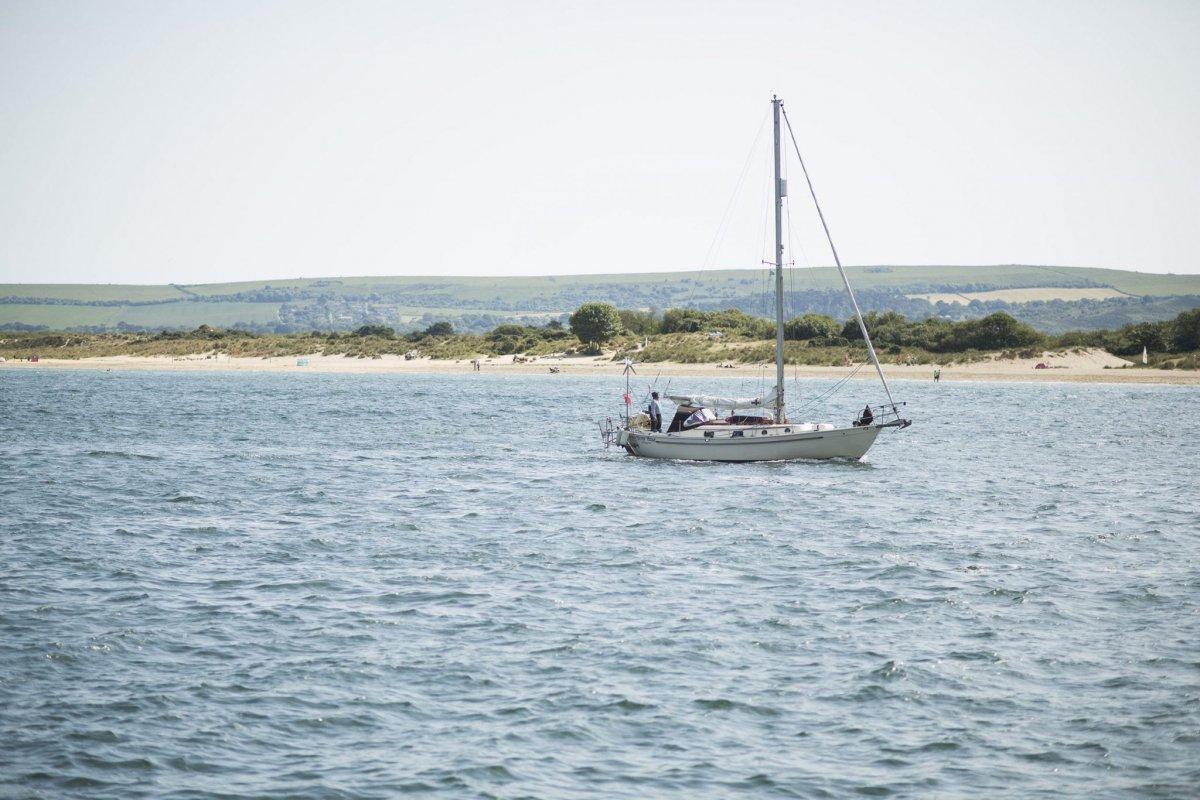 A lone boat bobbing in the sea. In the background is a flat strip of Studland's sandy beach with rolling green hills in the far distance.