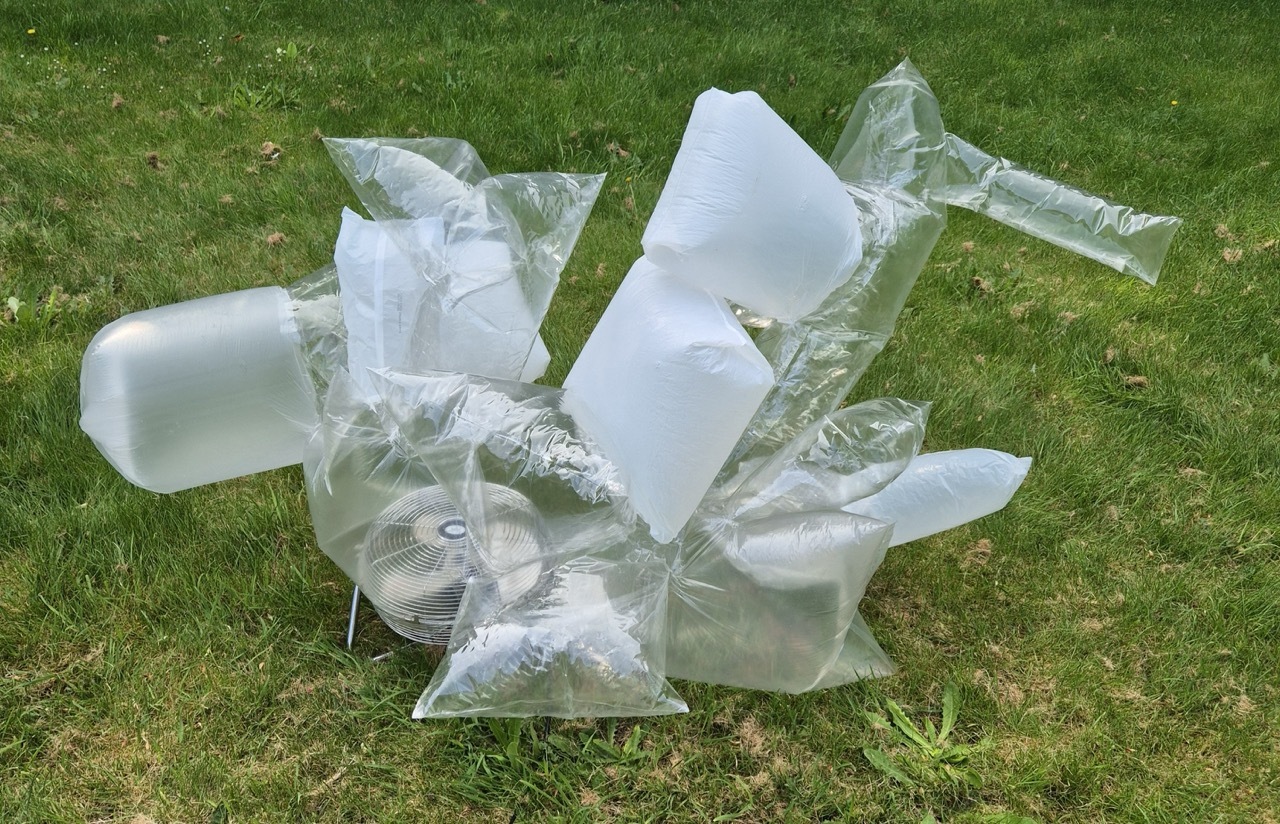Clear and white plastic bag sculpture on green grass lawn, blown up by a fan.
