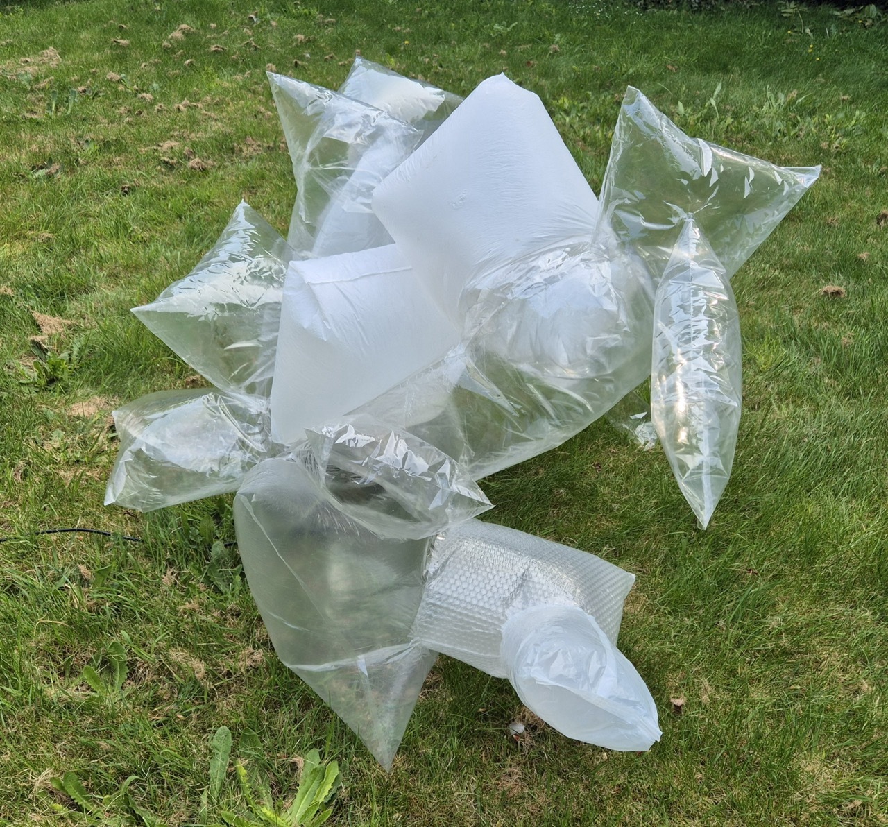 Clear and white plastic bag sculpture on green grass lawn, blown up by a fan.