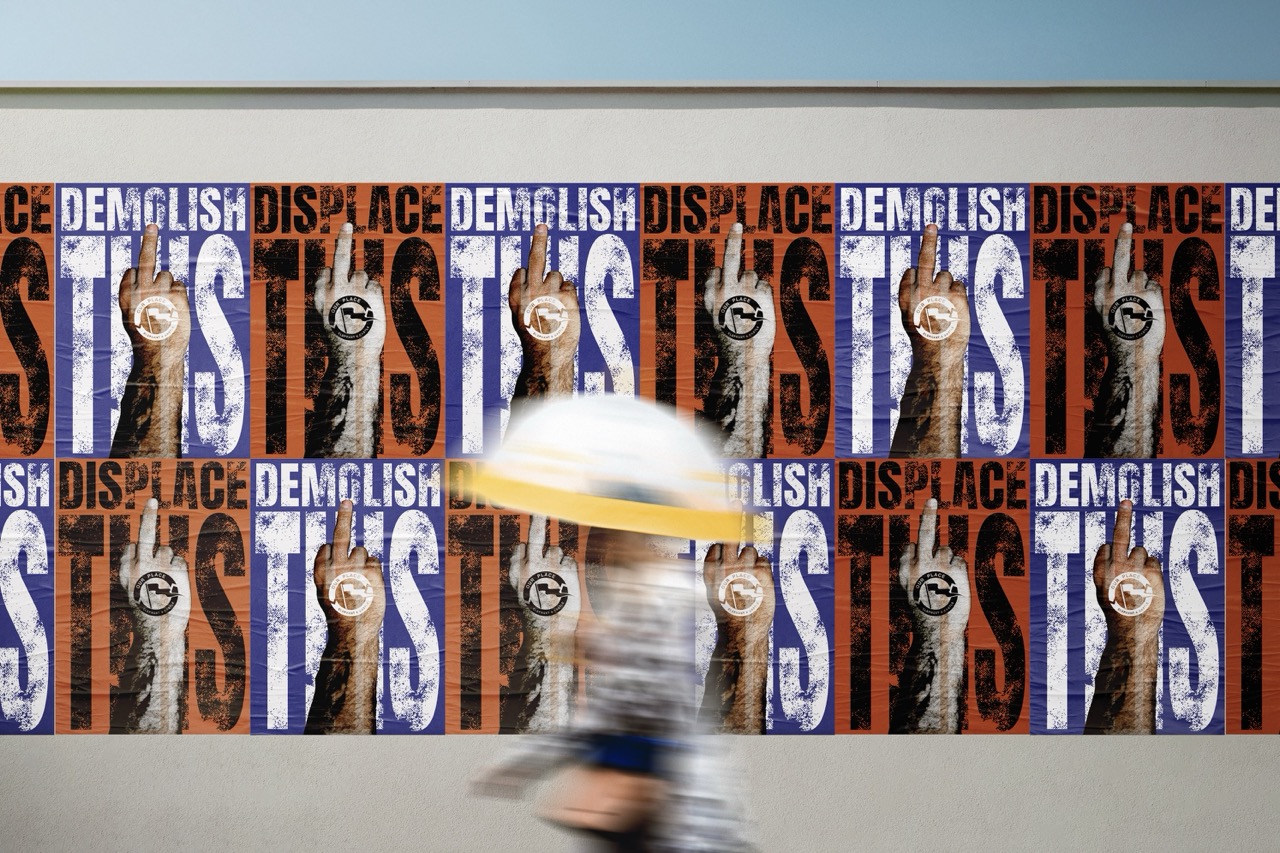 Mock-up posters in orange and purple that read 'Demolish this' with a hand giving the middle finger, blurred person walking in front.