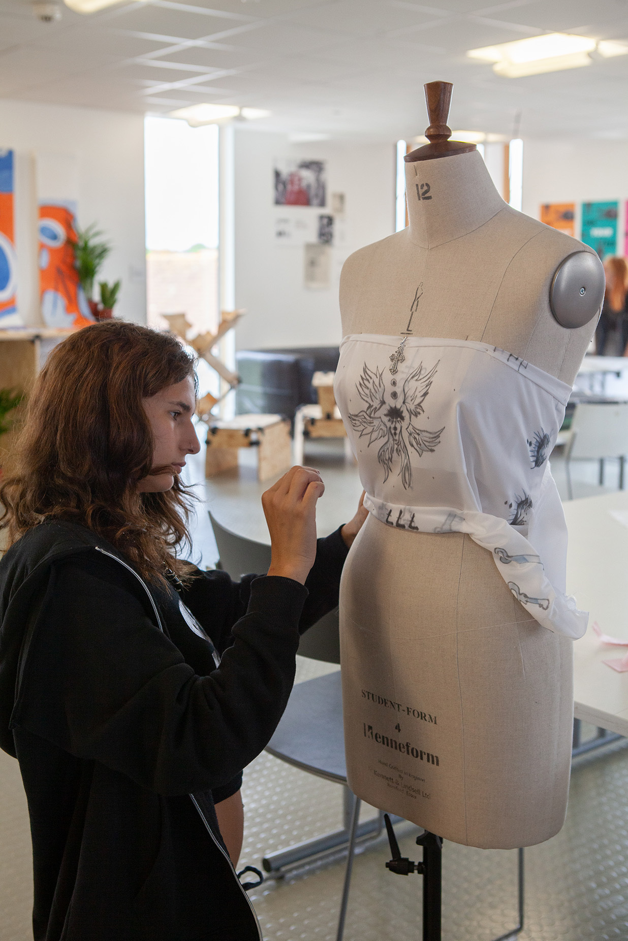 A student is pinning a design to a fashion mannequin
