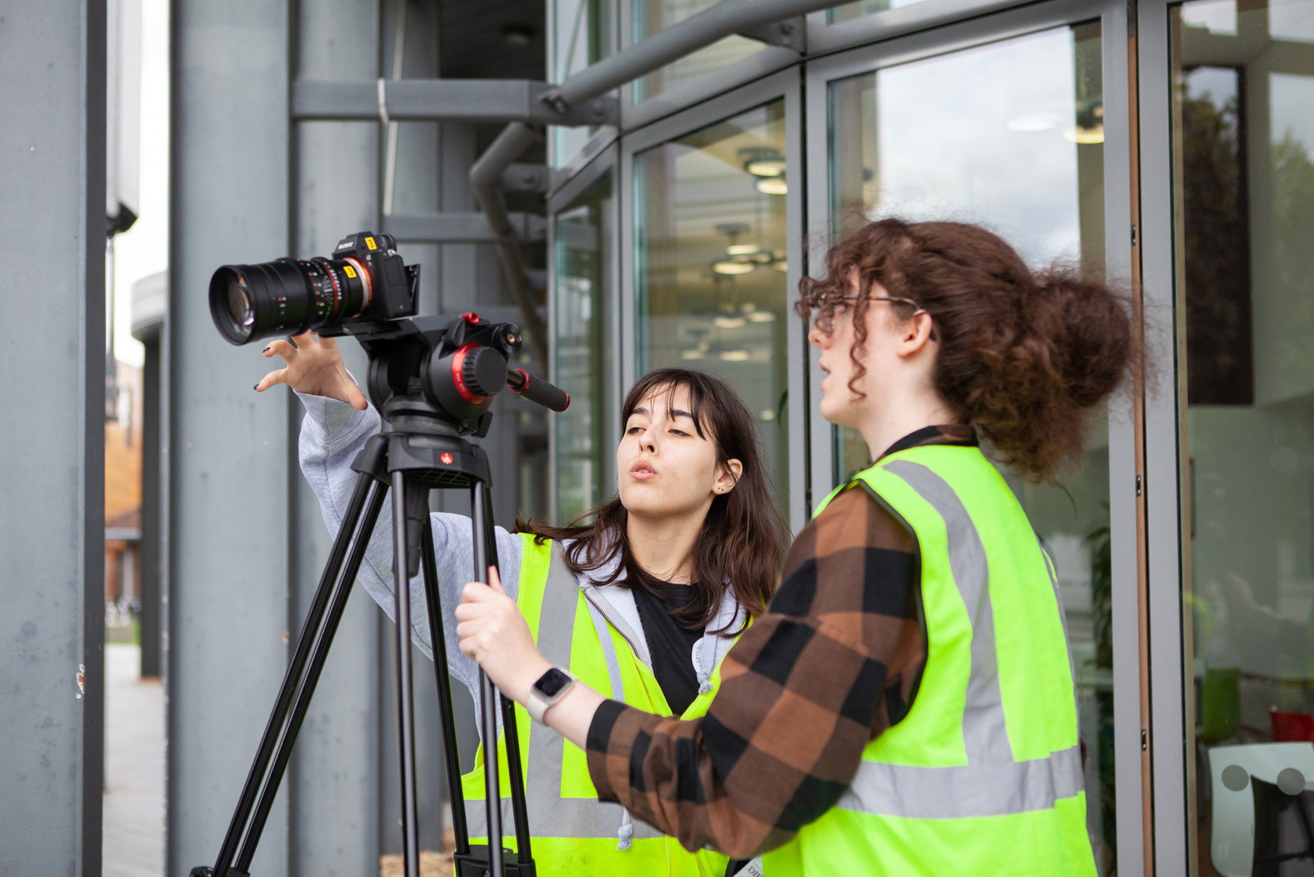 Two students wearing high vis jackets operating a camera