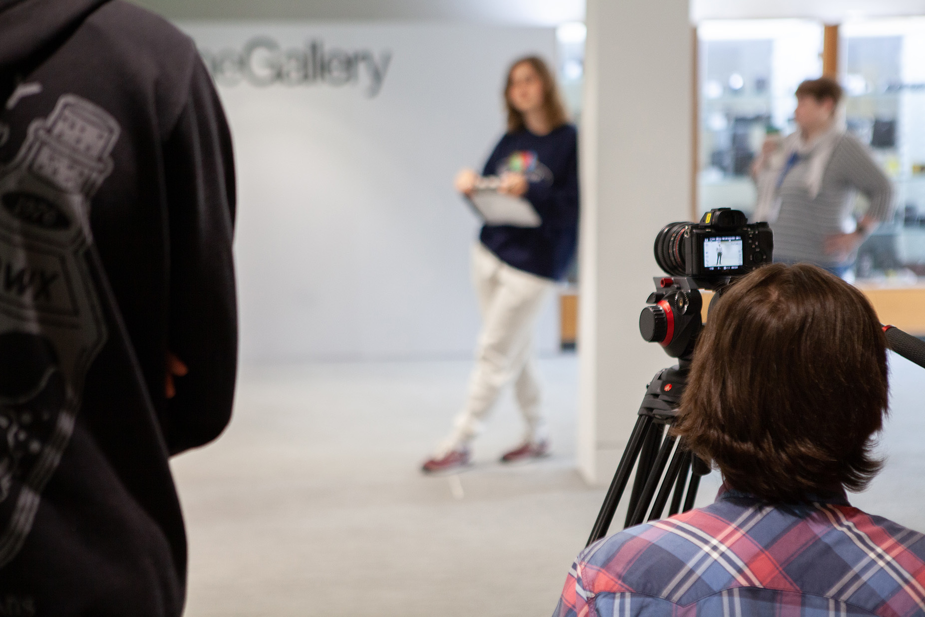 Student using a camera to film an actor walking down the corridor