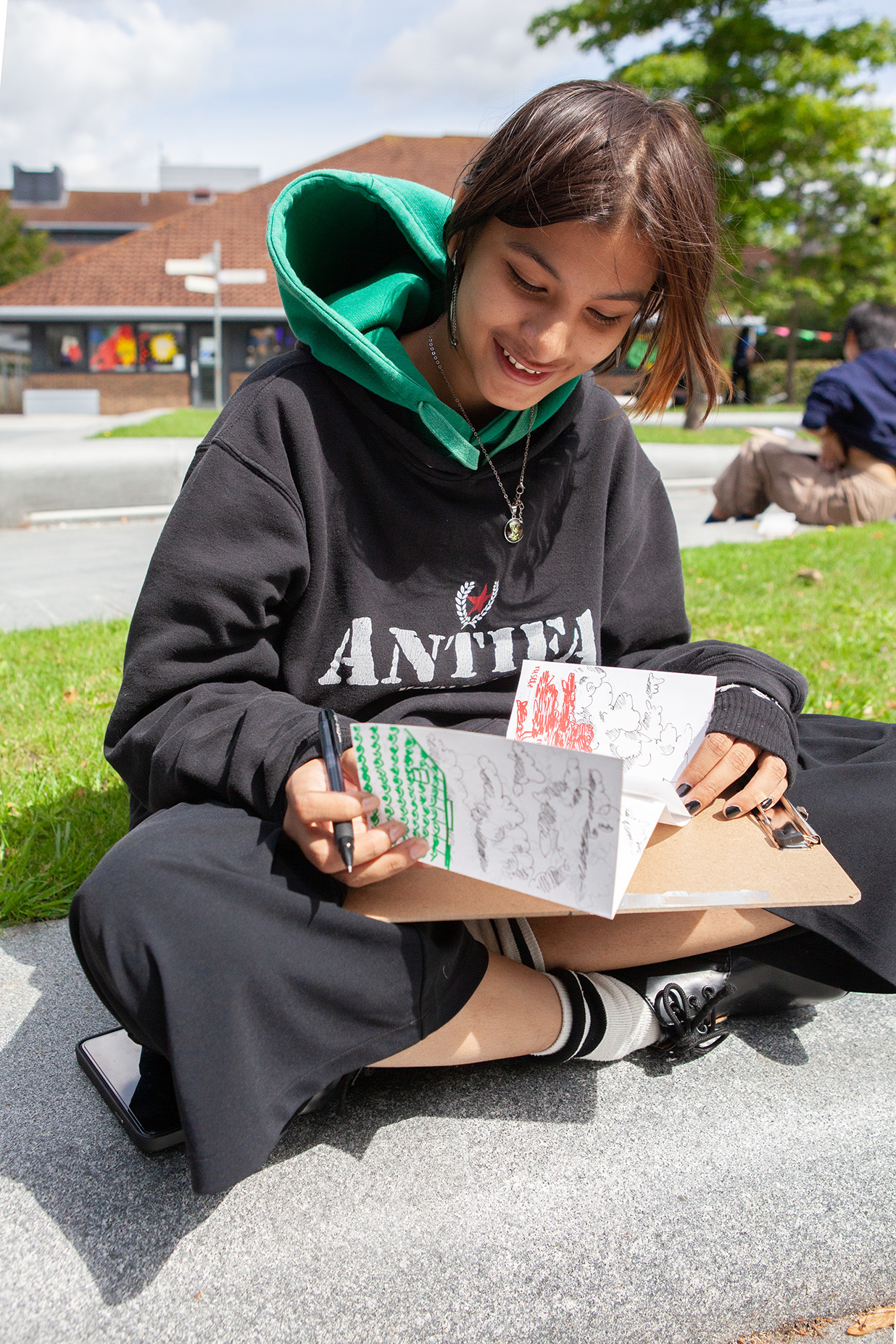 A student is sat on the grass drawing in their sketchbook