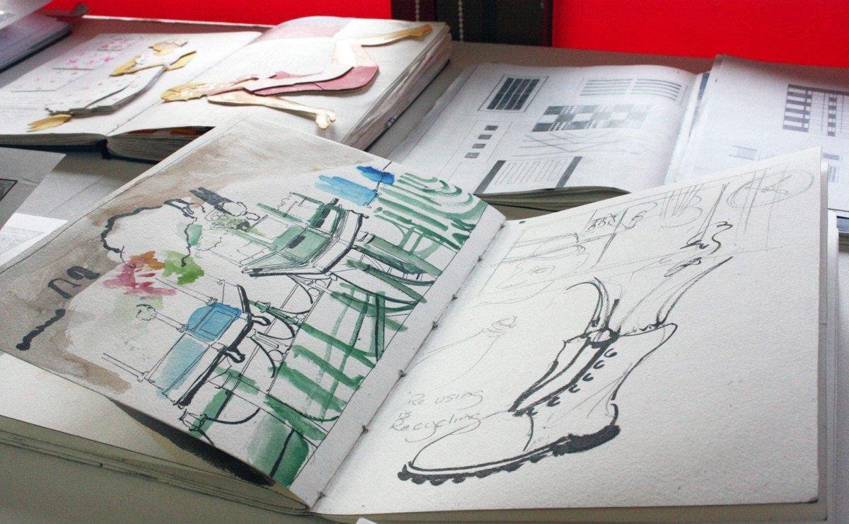 Three portfolio books open on a table to show double-page spreads with artwork, diagrams and other work.