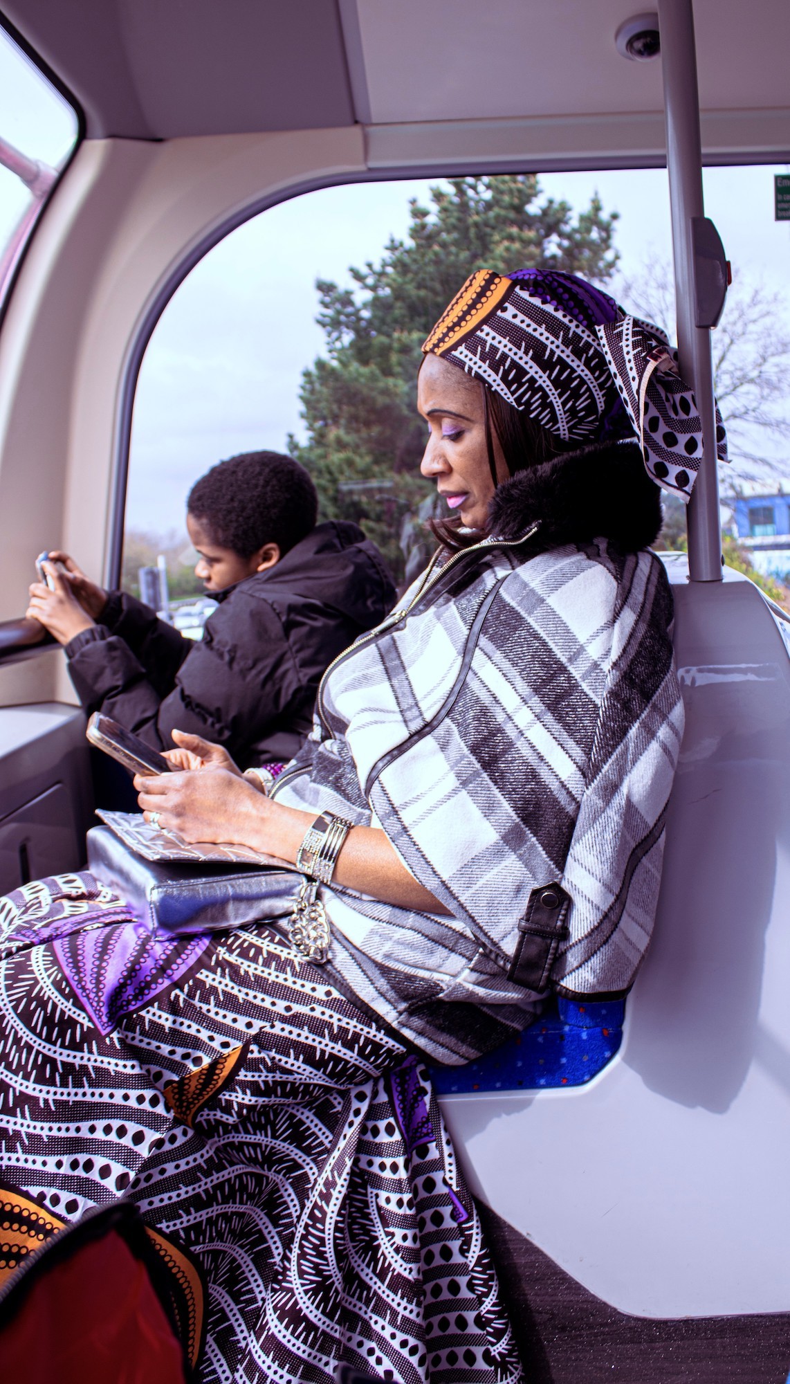 Portrait of a mother and son sitting at the front of the top deck of a double decker bus, both playing on their phones.