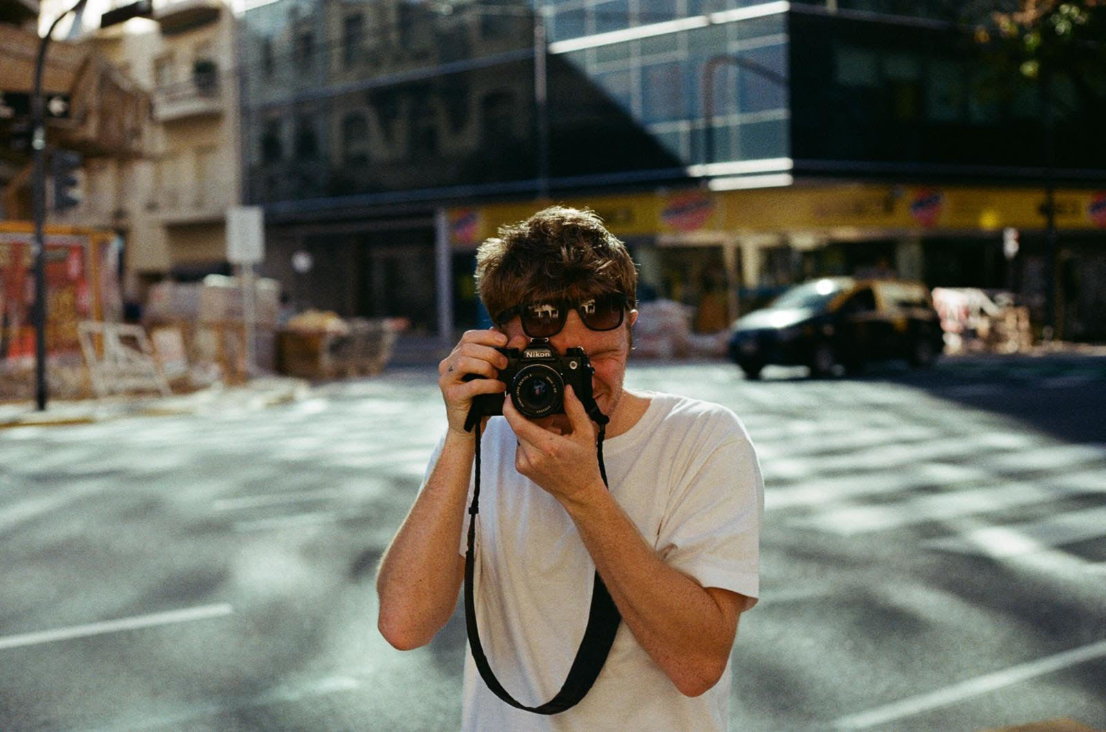 Mitch Payne taking a photo of the camera's perspective, in front of an urban background.