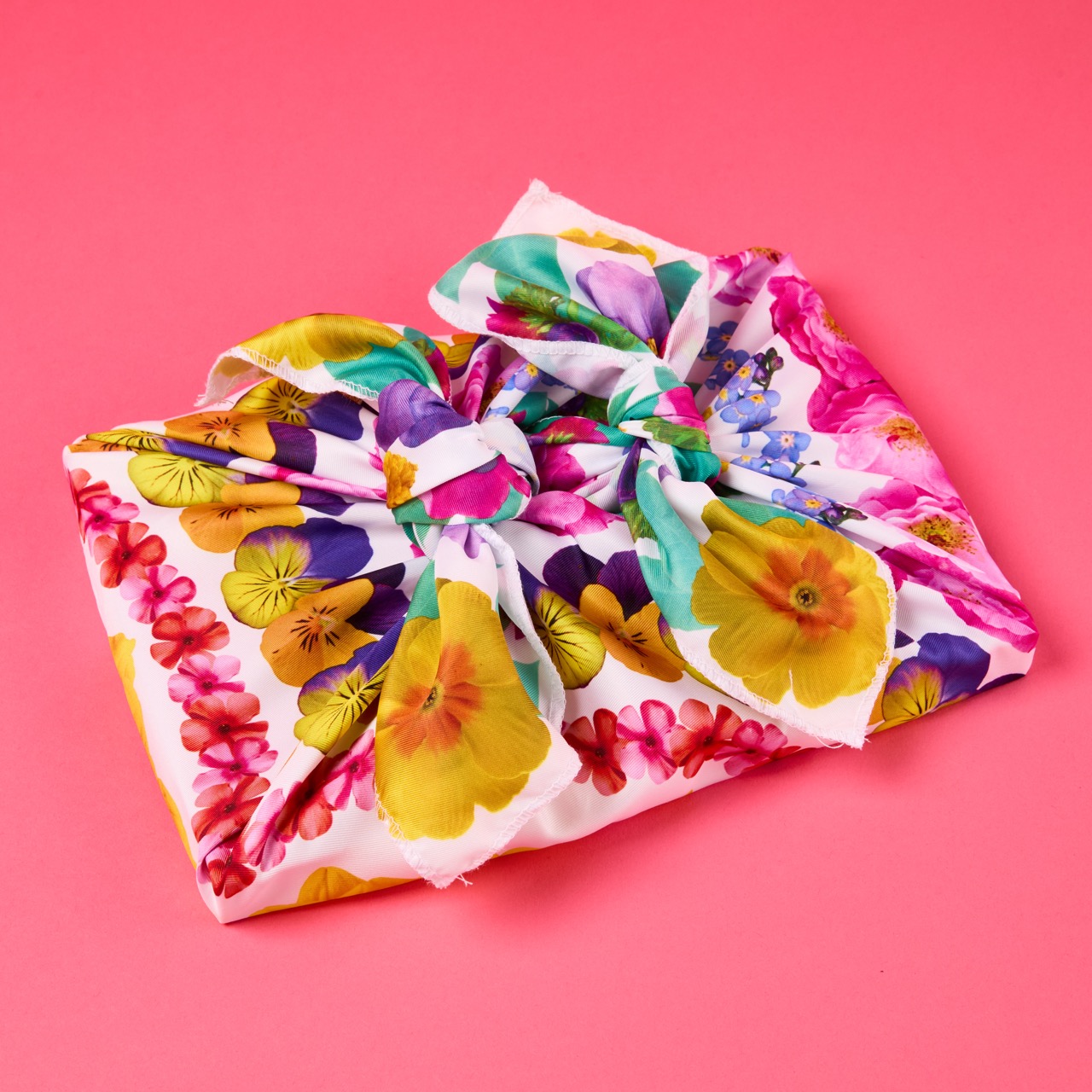 Multicoloured, pattered Lush Knot Wrap on a bright coral pink/red background.