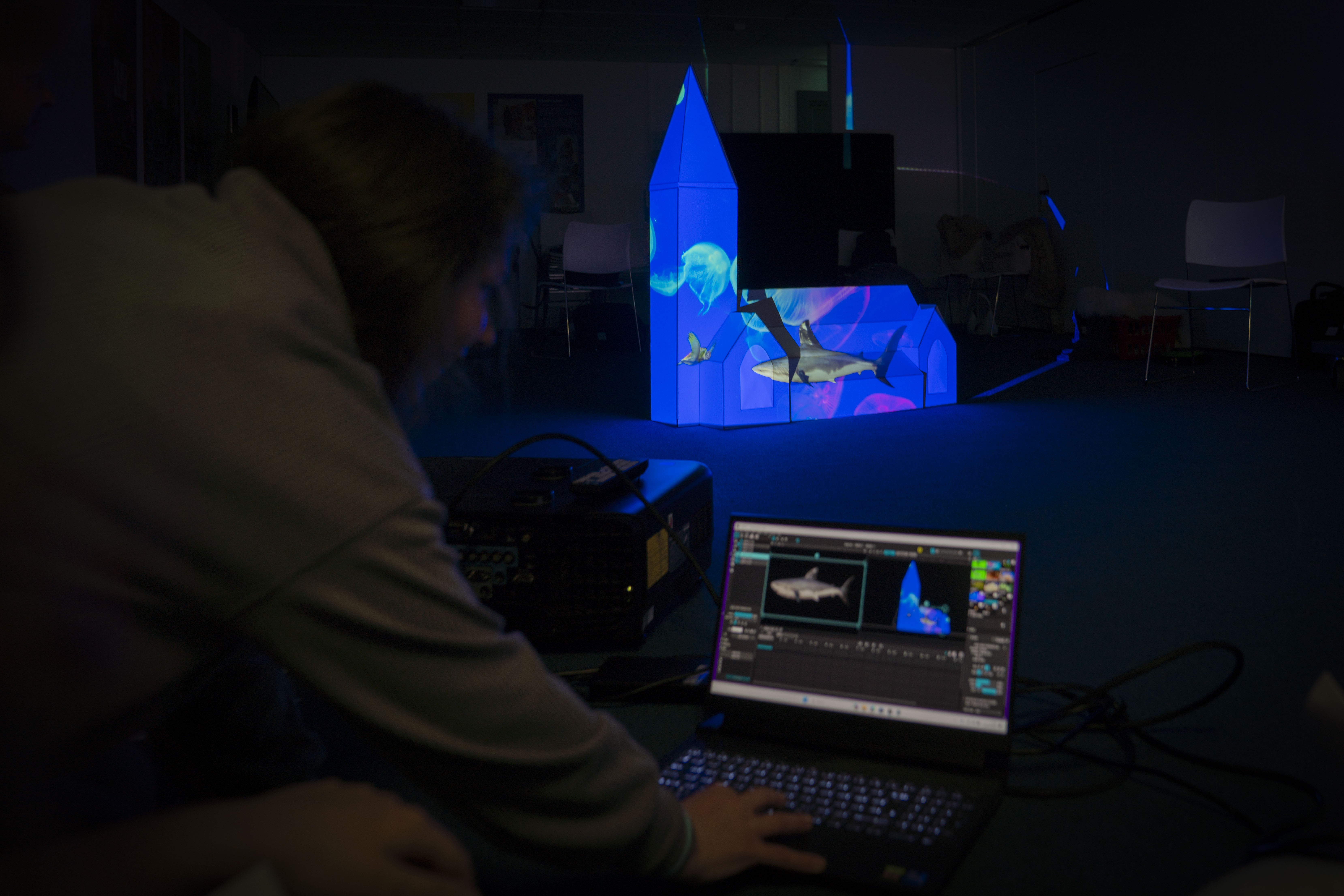 Mock-up church model with blue light and images projected onto it, person working on a laptop in front.