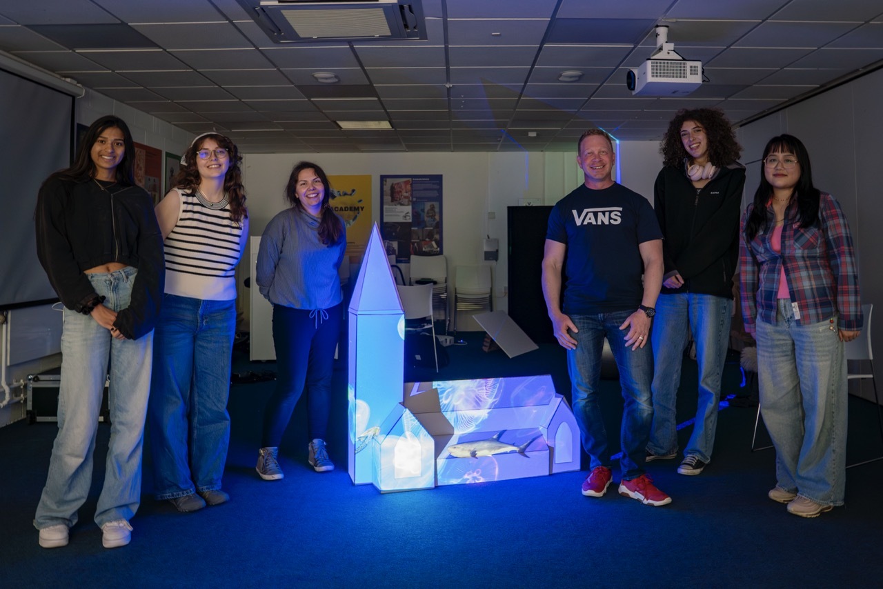 Students and projection mapping team stood around a mock-up church model with blue light and images projected onto it.