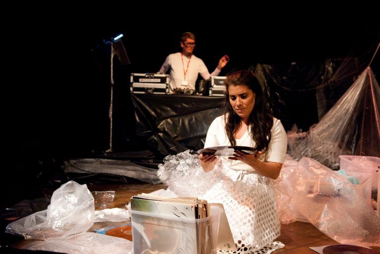 A person kneels by a box of records and examines a vinyl disc.