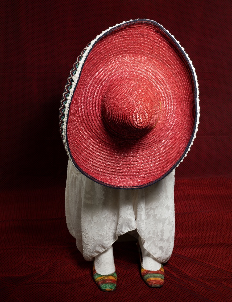 Studio shot of a model wearing a red sombrero, face obscured, red background.