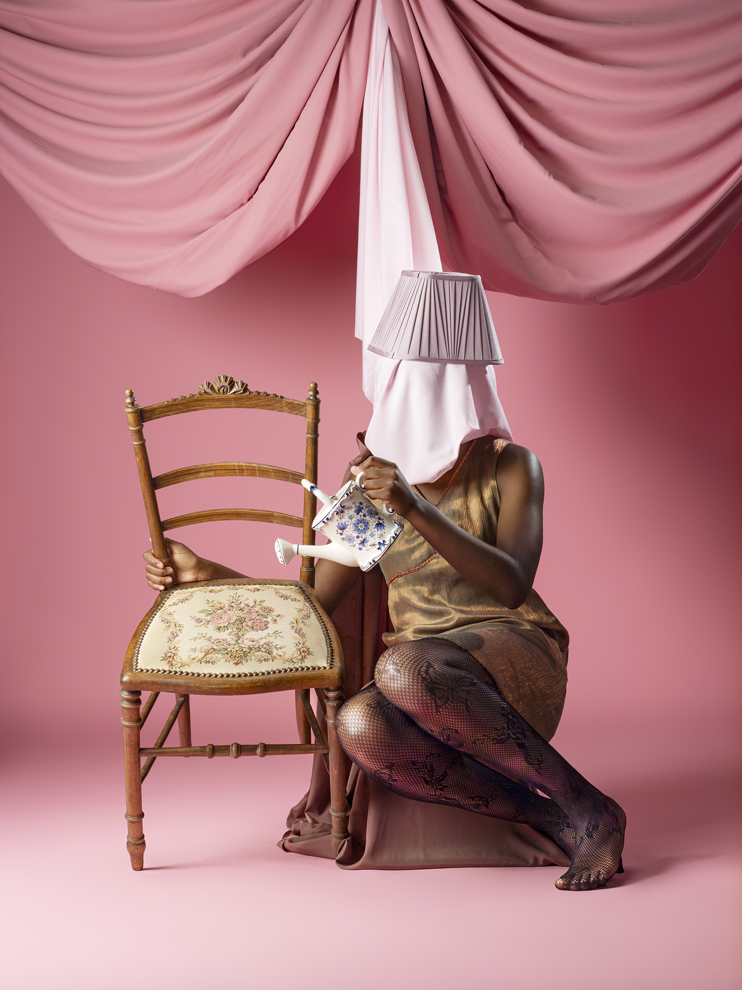 Uncanny Fashion photoshoot featuring a model on a chair wearing and holding thrifted items, pink background.