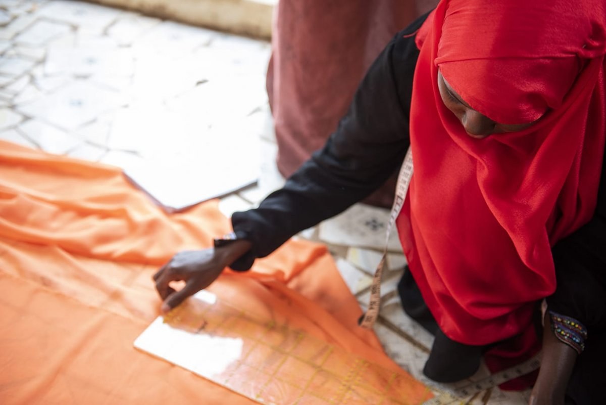 A person wearing a hijab lays down a roll of fabric on the floor and takes a measurement