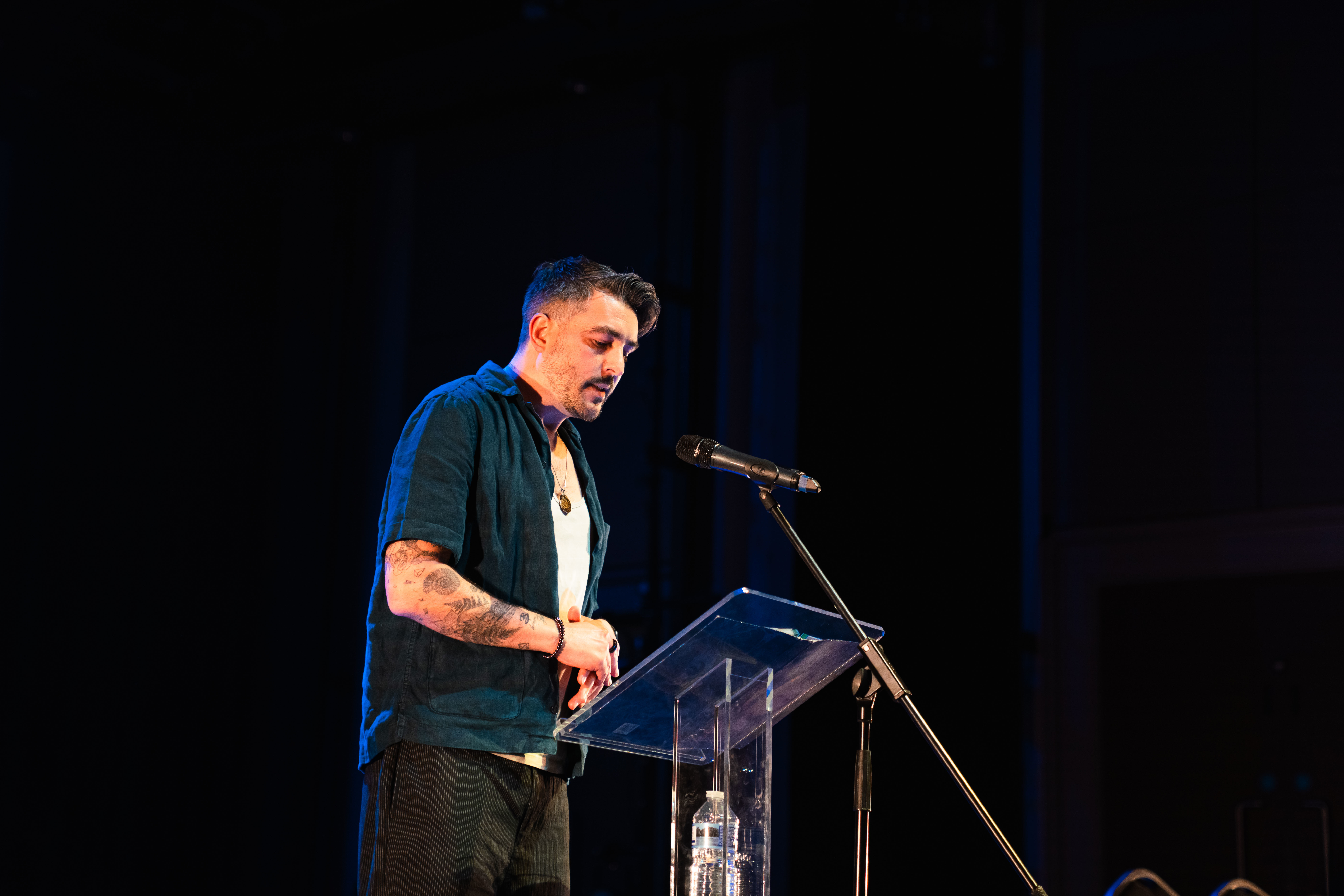 Dr J Cole, course leader of BA (Hons) Creative Writing at Arts University Bournemouth, standing at a lectern on a stage, performing at Bournemouth Writing Festival.