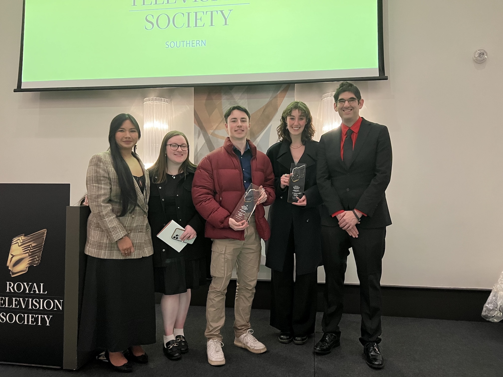 BA (Hons) Animation Production graduates N Busschaert and V Draghi standing with other team members and an official at the Royal Television Society Southern Awards.