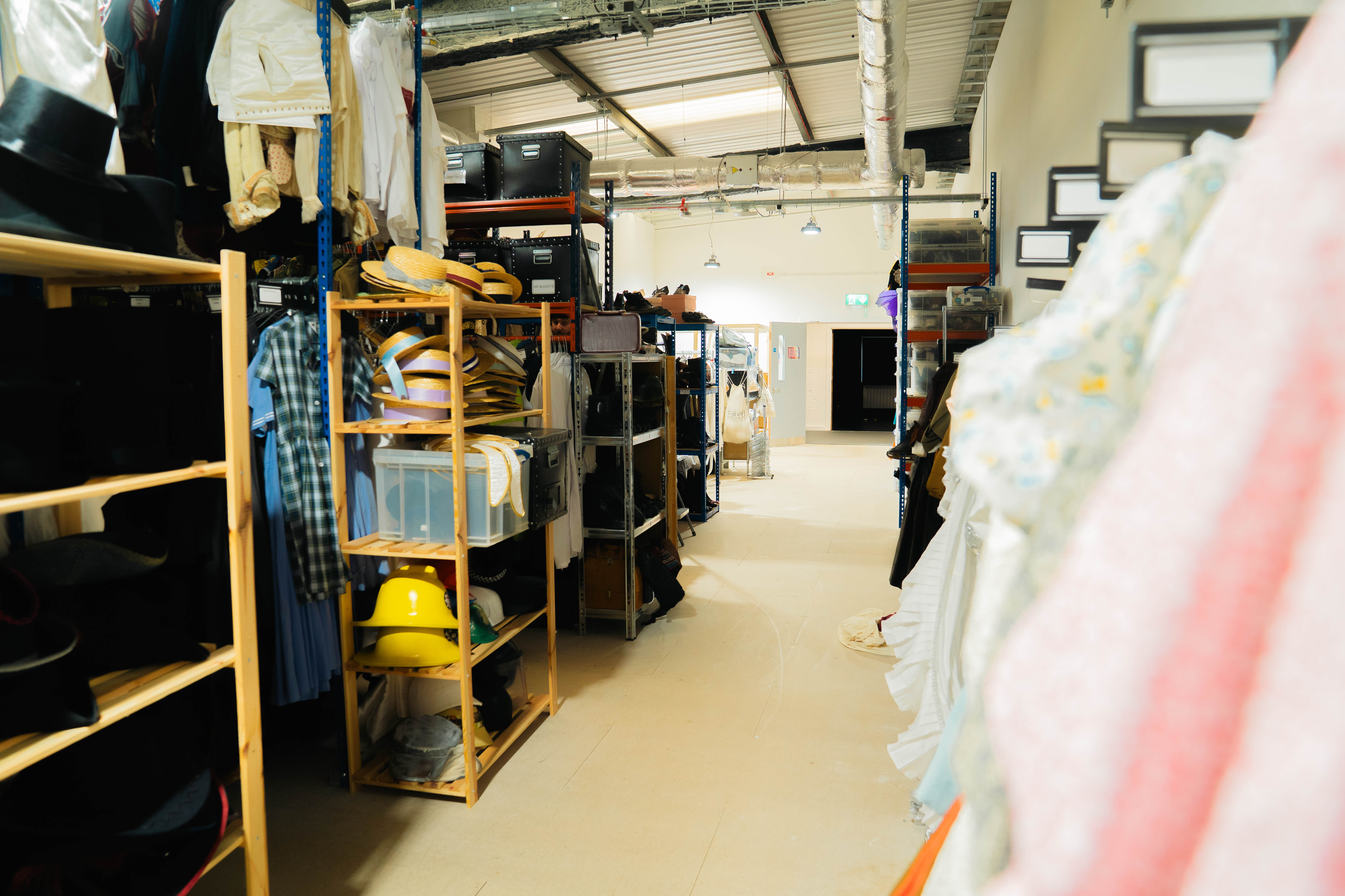 Industrial warehouse interior with metal shelving units, stored materials, concrete floor, and overhead lighting fixtures.