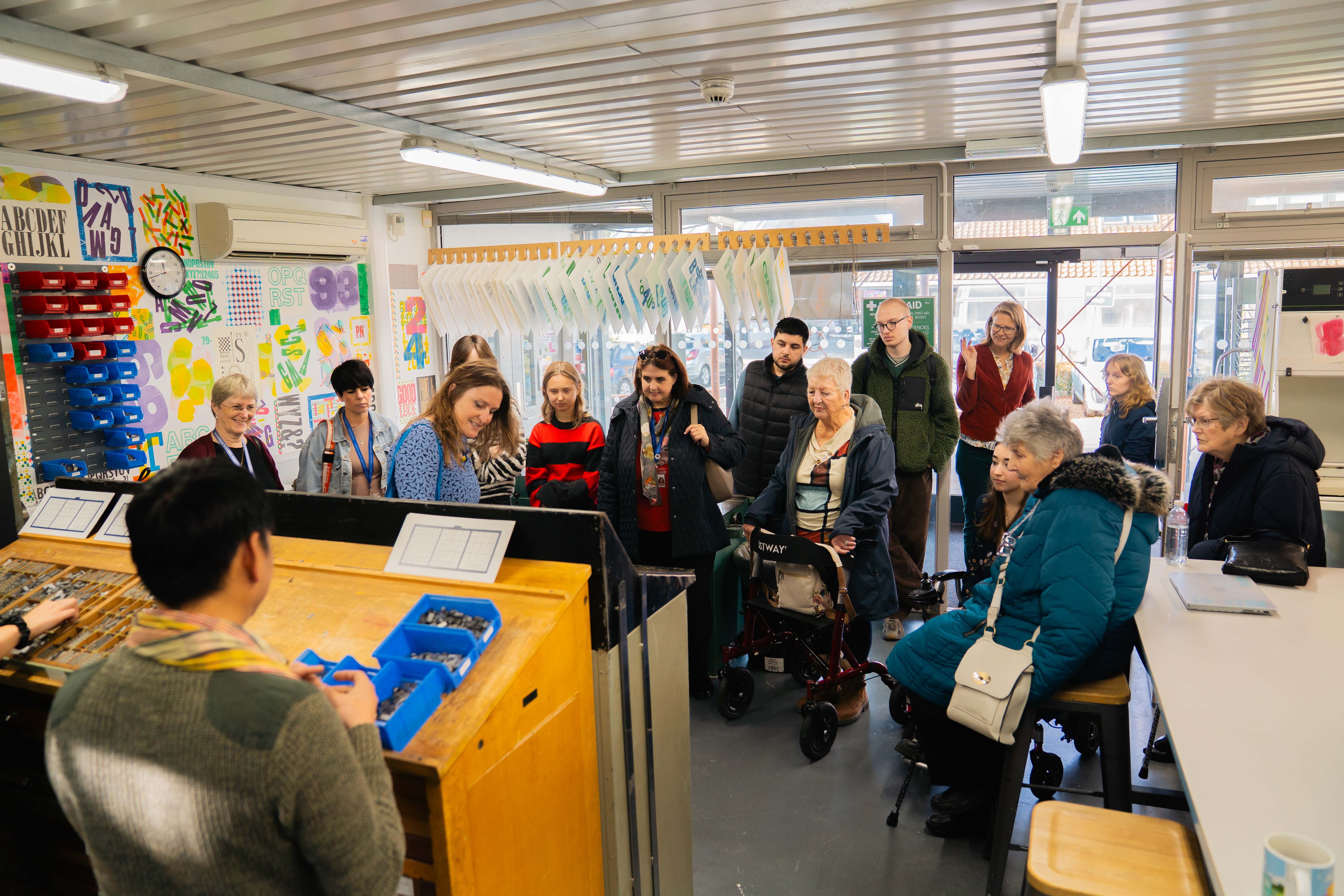 Group of elderly people gathered in classroom watching man at wooden podium with microphone and laptop.