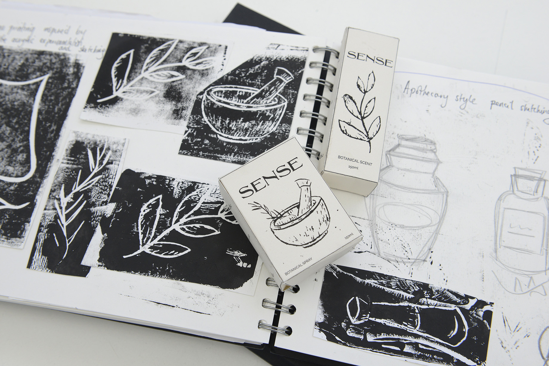 Two pieces of packaging for 'Sense' lie on the spine of an open sketchbook.