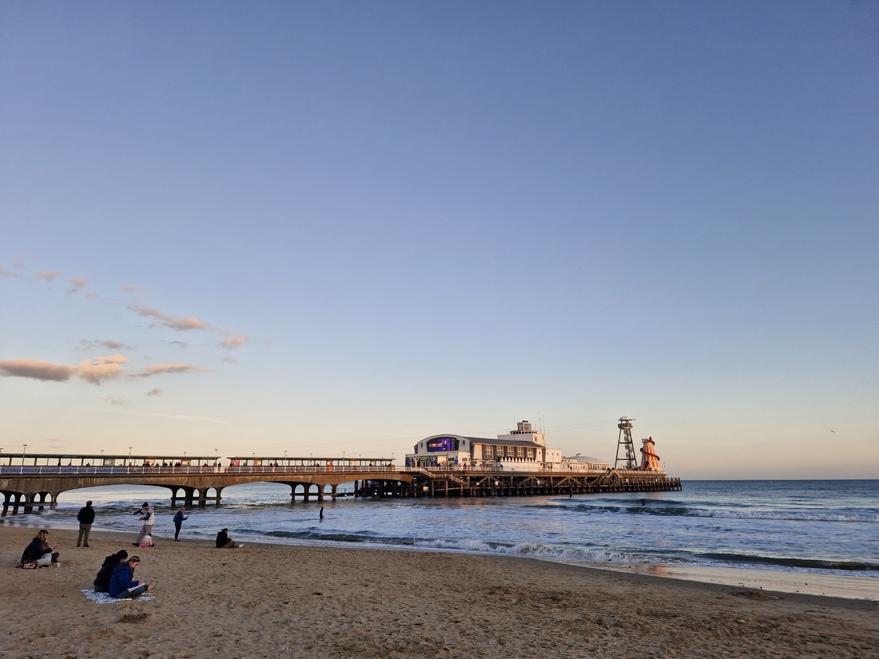 Bournemouth Pier at sunset, blue-orange sky and people sat on the beach or swimming.