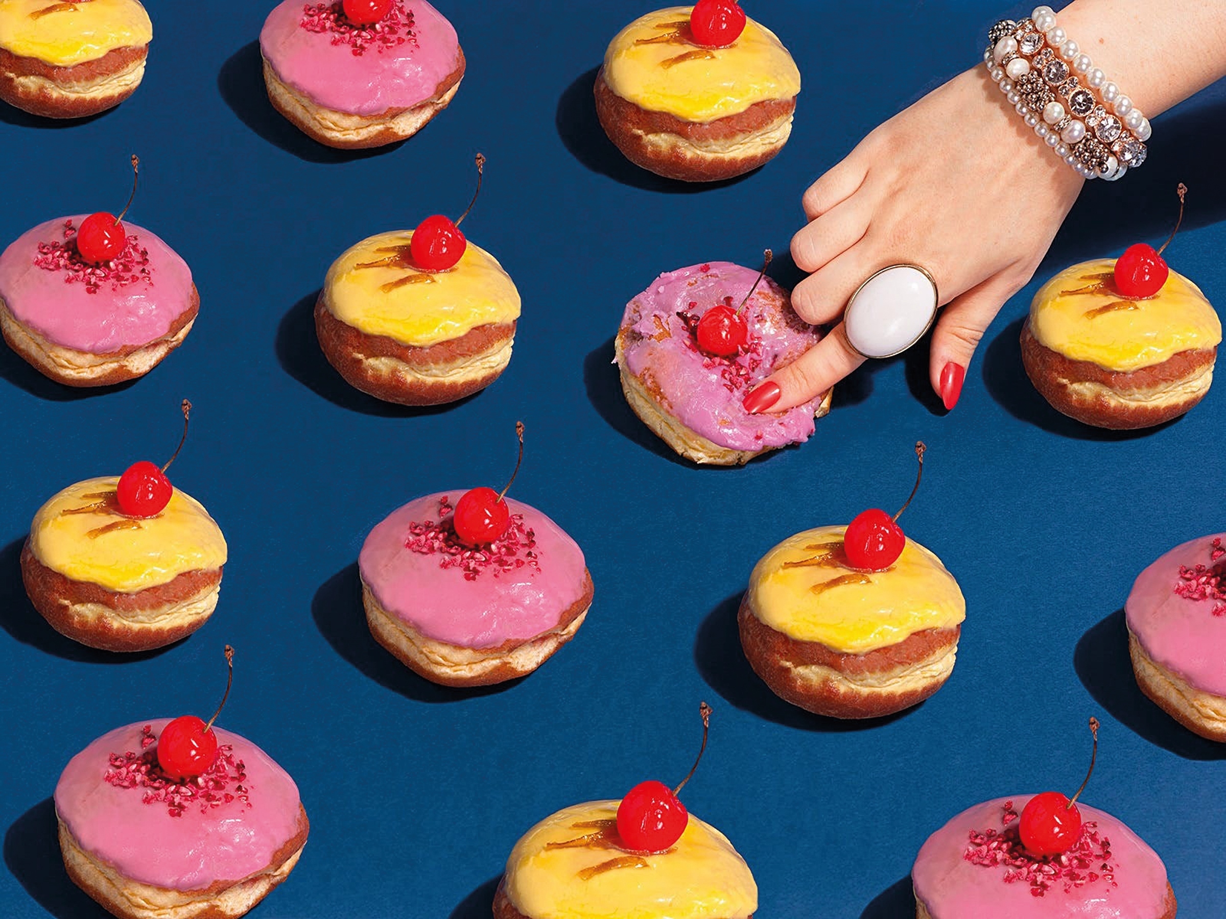 Yellow and pink doughnuts lined up in rows, a hand is coming in from the top squashing one with an index finger