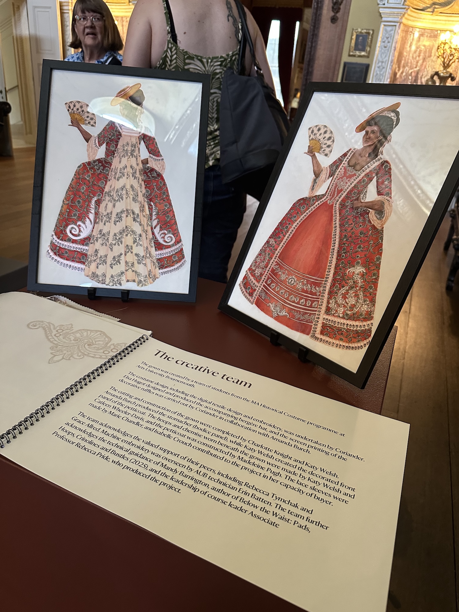 Two framed illustrations of a person wearing an ornate patterned red and white dress and a gold train, with a book open to a page entitled "The creative team" in the foreground.