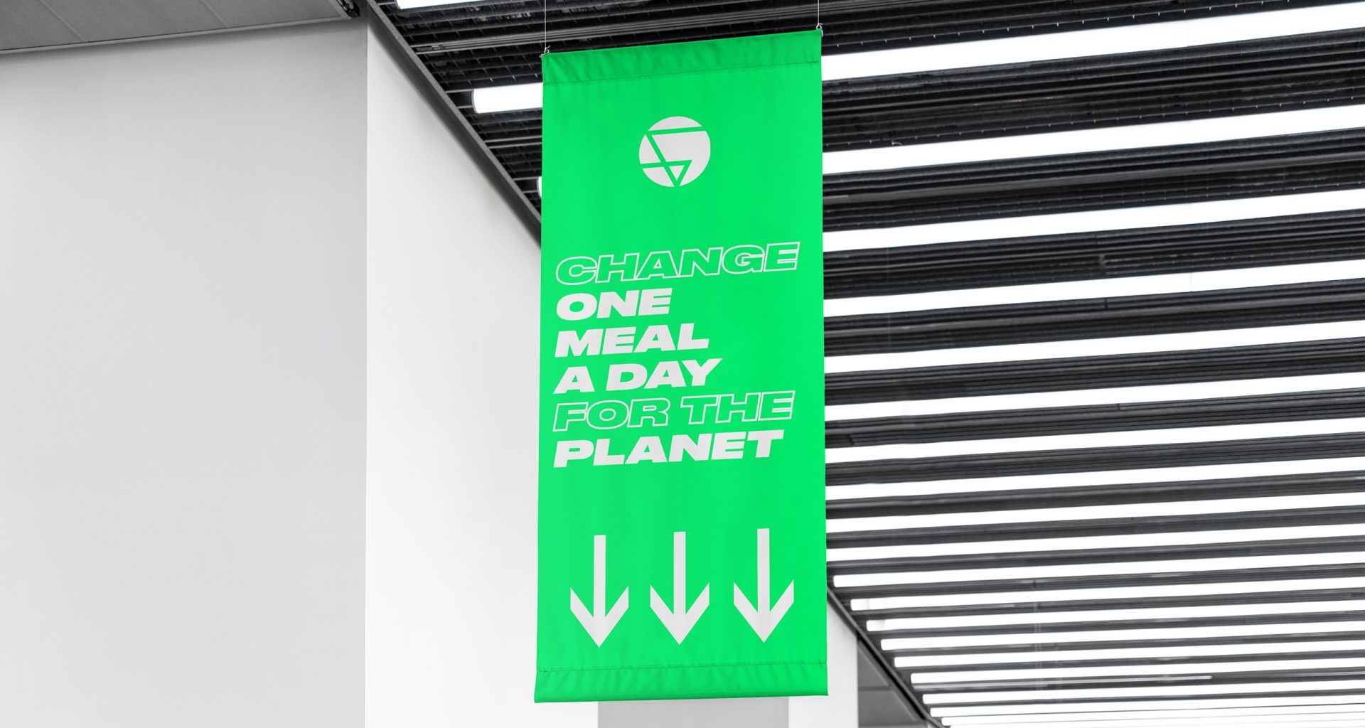 A green banner hanging from a ceiling with the text 'Change one meal a day for the planet' and three downward arrows underneath.