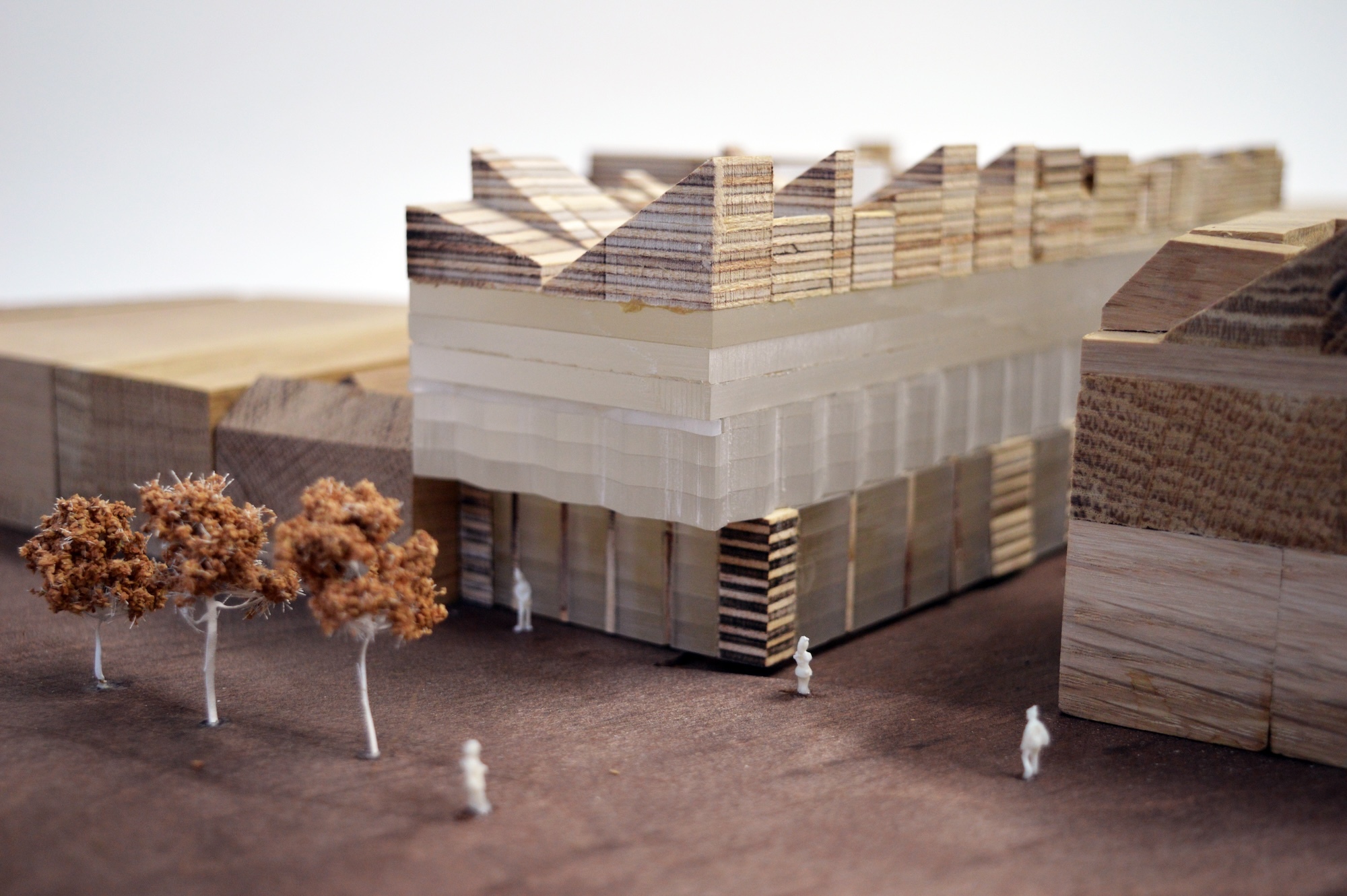 Close-up of an architectural model of a building made up of resin and wooden blocks, with three trees and several figures in the foreground.