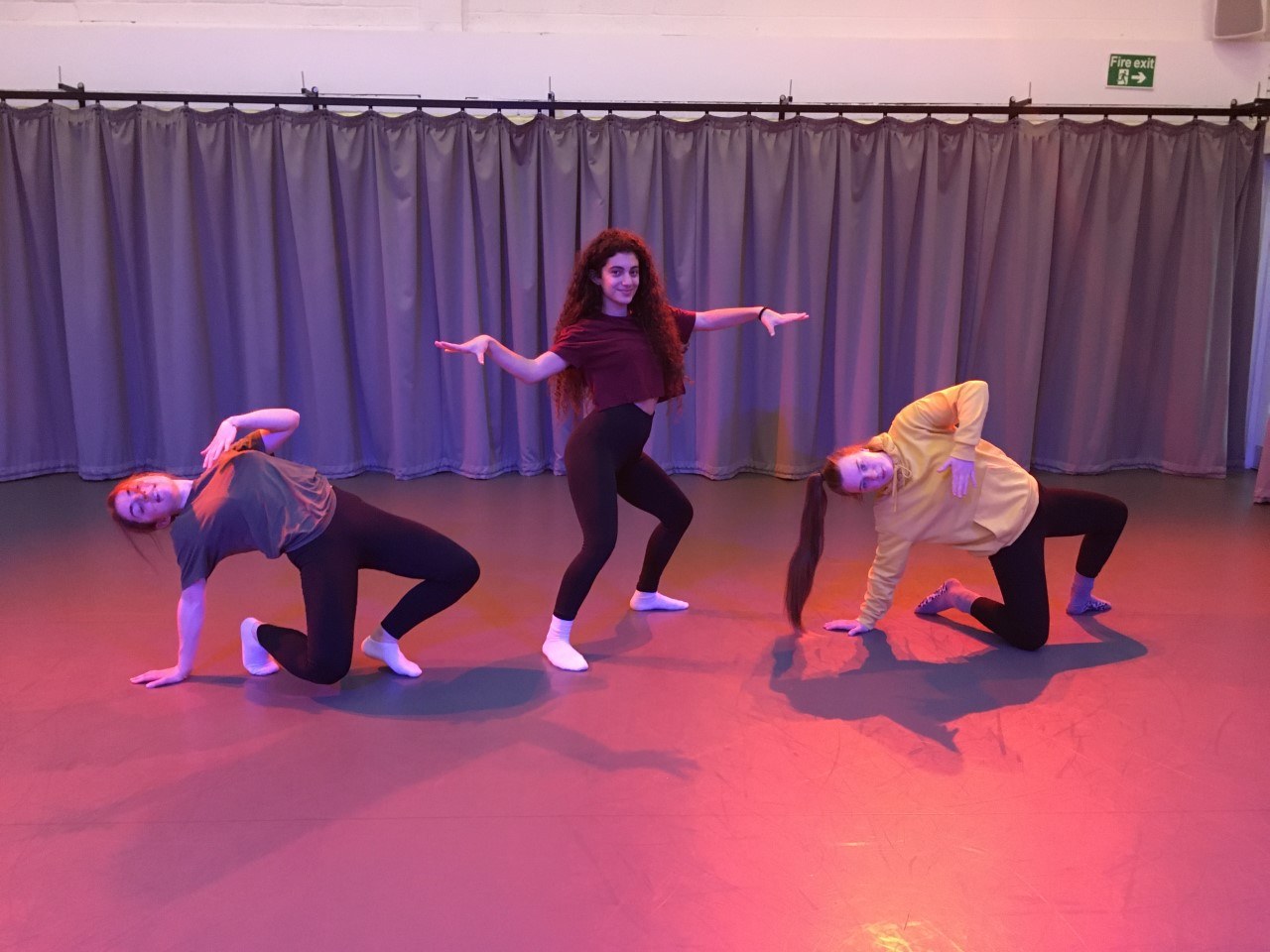 Three BA (Hons) Dance students rehearsing in a dance studio with a long stretch of curtains in the background.