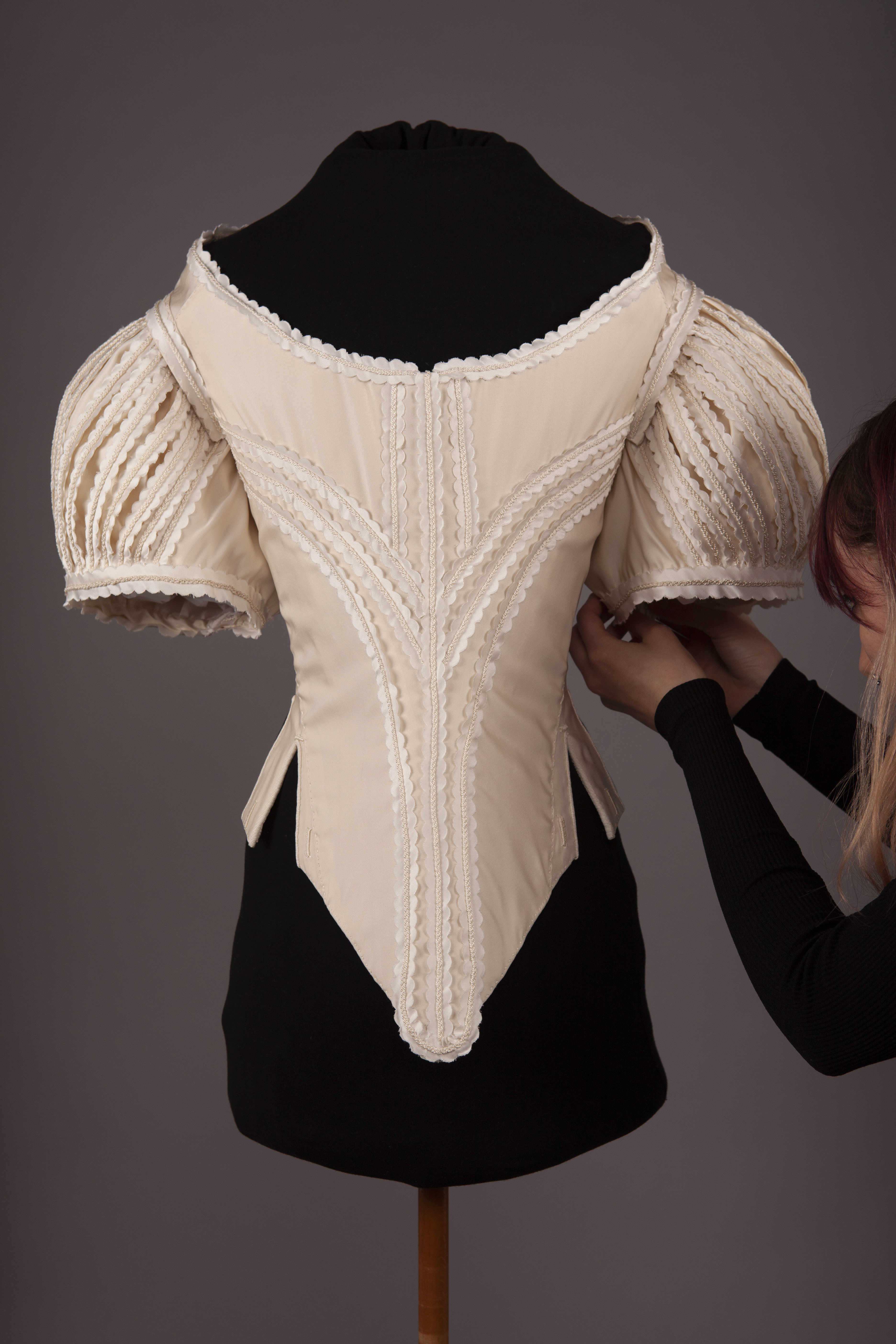 A BA (Hons) Costume design student adjusts the sleeve of a 1660s bodice on display on a mannequin.