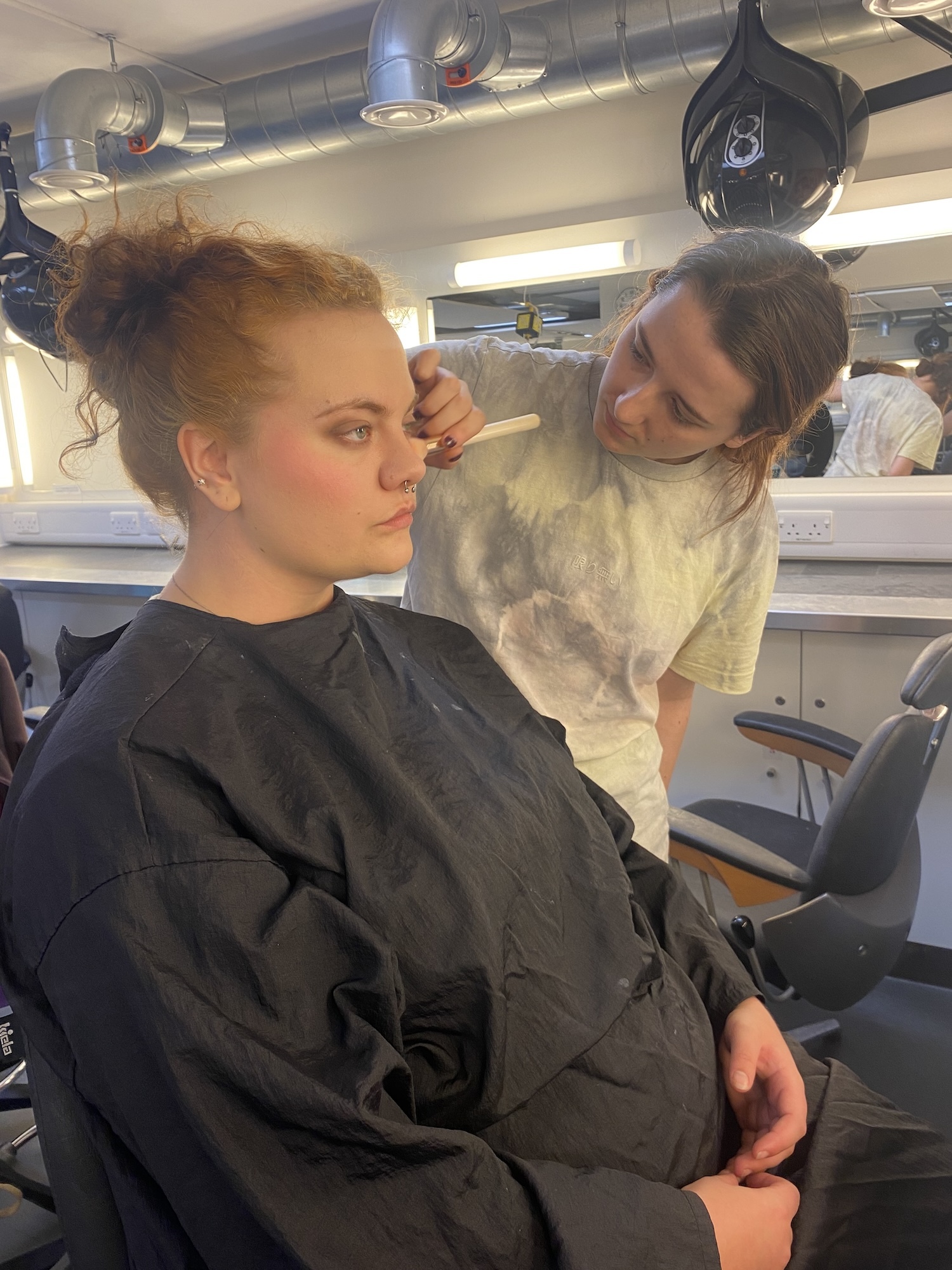 An AUB student sits in a black smock having their make-up done by another student.