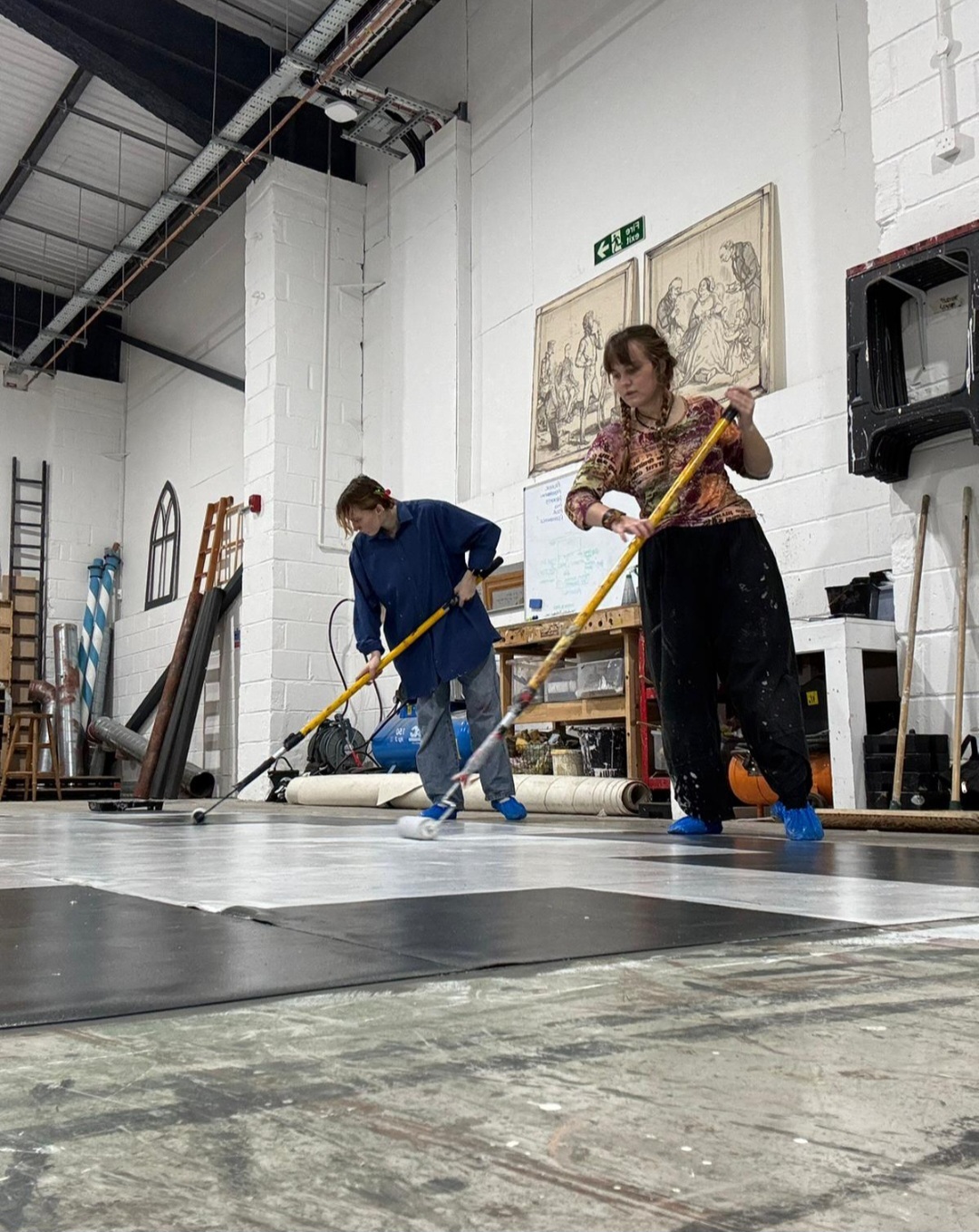 Two students working with large paint rollers painting a set's flooring at Elliott Road Studios.