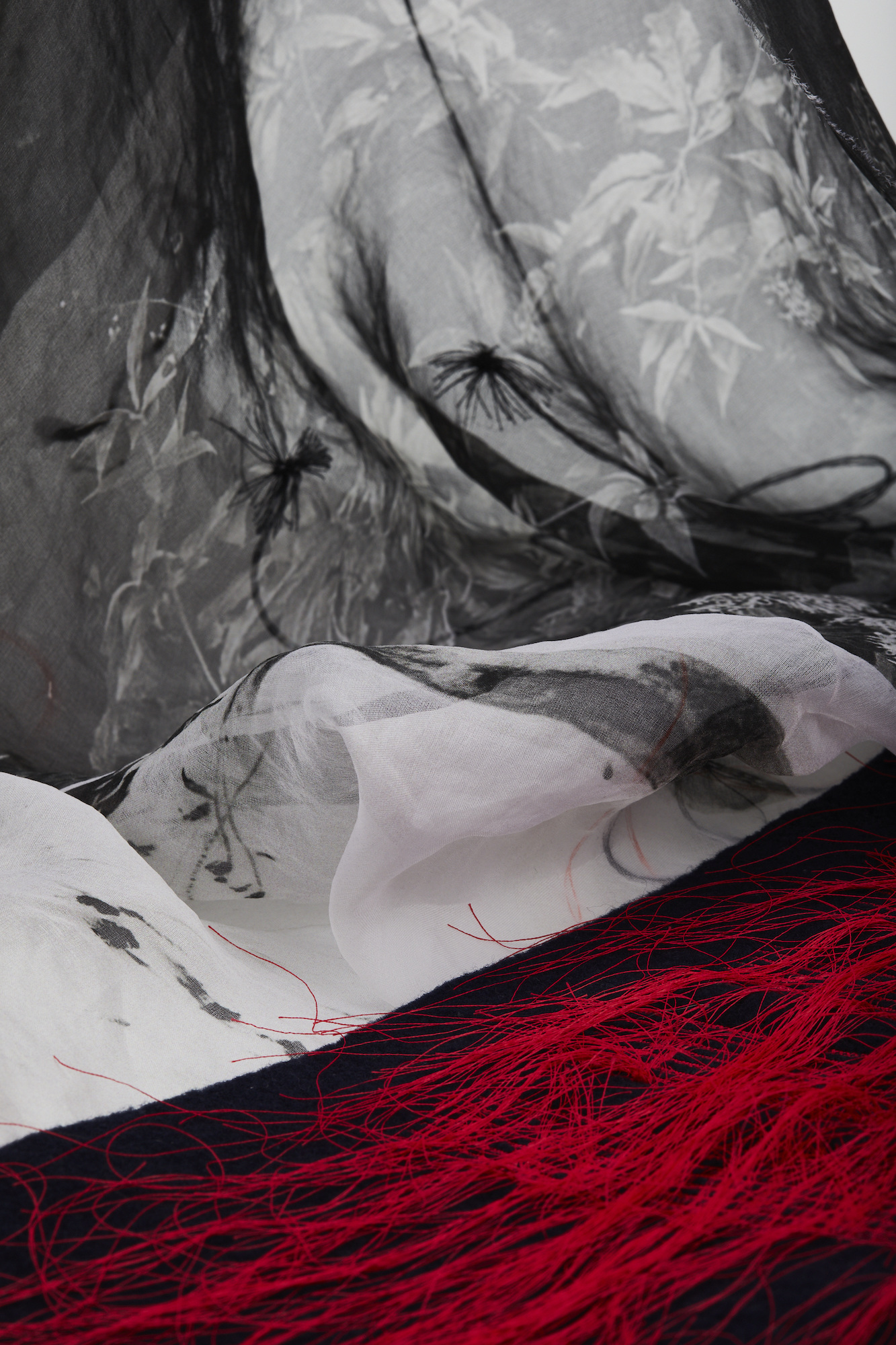 Black, grey and white plant-patterned fabrics, some with red feather trimming, on display.