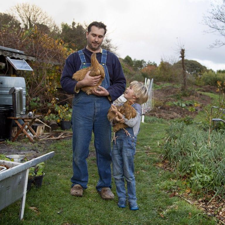 Man standing with a child next to them looking up. Both are holding chickens.