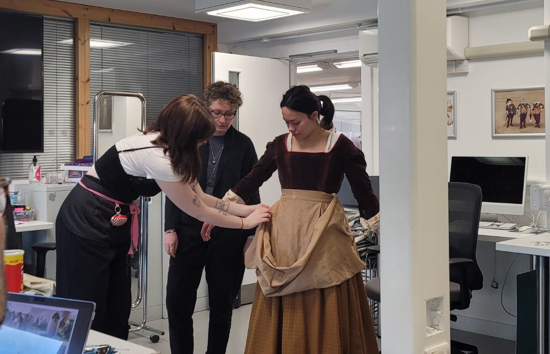 Students working on a period costume worn by a model, brown and red velvet.